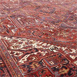 North West Persian Heriz hand-knotted carpet, madder red field with central bold angular steeped medallion with serrated outlines, flanked by stylized palmettes, hooked leaves and geometric motifs, spandrels similarly decorated within a wide geometric border and multiple guard borders in tones of madder red, indigo blue, ivory and olive green, with cotton fringe ends  