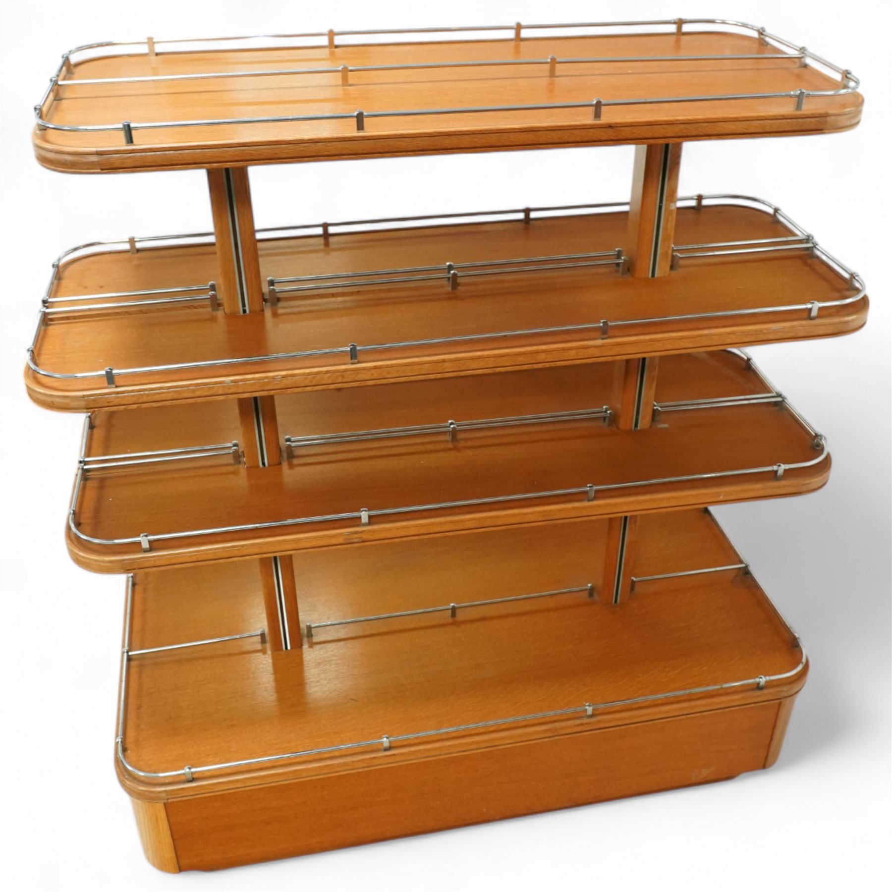 Mid-20th century retail display stand, of stepped rectangular tiered form with four graduated adjustable shelves, each with rounded corners and fitted with tubular chrome safety rails, supported by central chrome-mounted wooden uprights over a plinth base