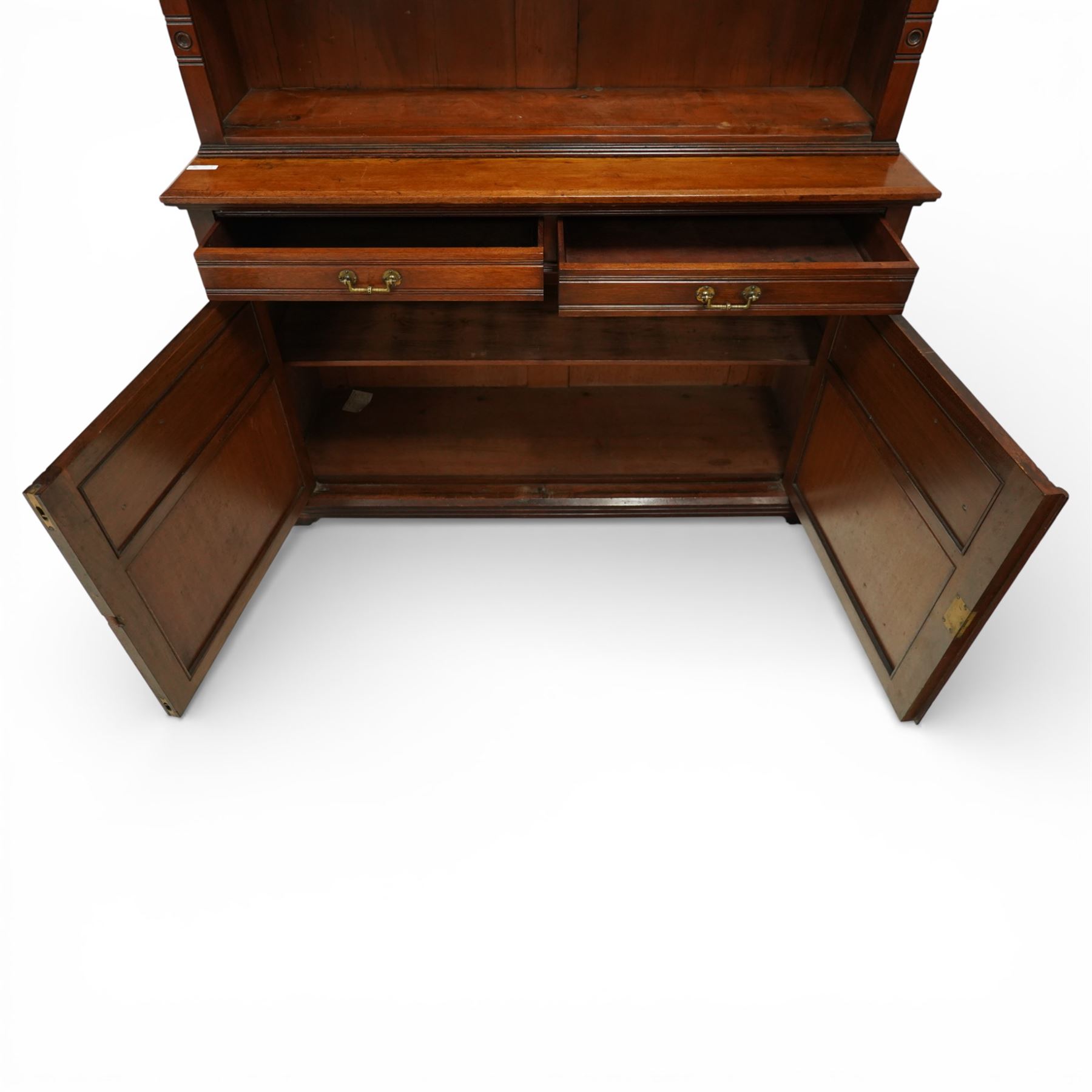 Late Victorian tall walnut open bookcase on cupboard, projecting cavetto cornice over reeded and fluted uprights moulded with roundel motifs, flanking two adjustable shelves, the base fitted with two drawers over panelled cupboards, carved with oakleaf and acorn motifs and grapevines, on bracket feet