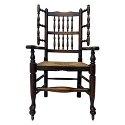 Early 19th century ash armchair, the back with winged spindles extending from a shaped top rail, above a splat of two rows of vertical spindles, with curved arms and a rush seat, raised on turned supports united by double stretchers terminating in castors