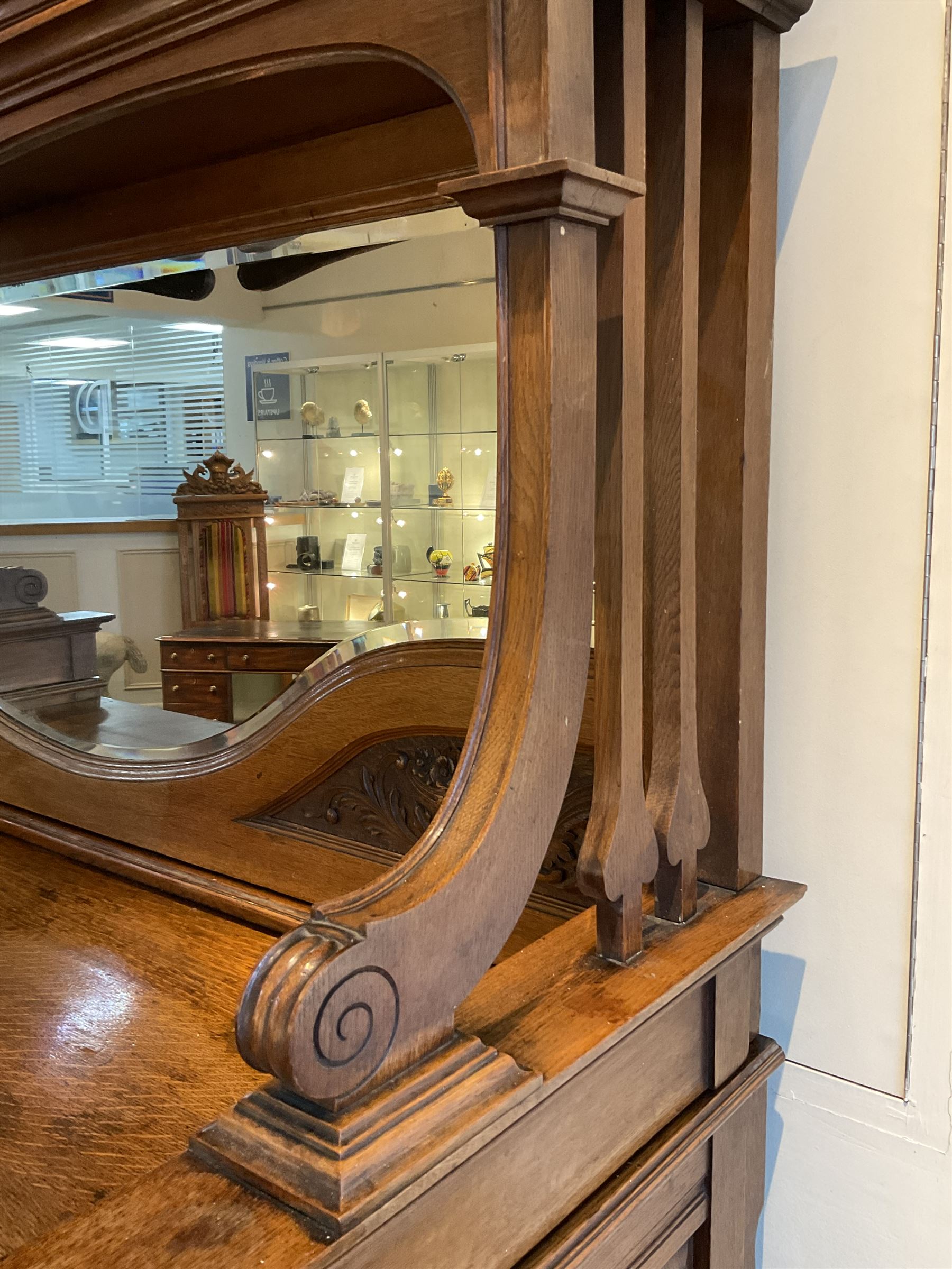 Late 19th century Arts & Crafts period oak mirror back sideboard, shaped bevelled mirror back carved with foliate scrolls and flower heads, down swept supports with elongated club-shaped uprights, moulded rectangular top over two drawers and three cupboards, the drawer fronts with copper handles decorated with sailing ships, panelled doors carved with mythical beasts, flowerheads and foliage, on moulded block feet