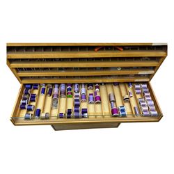 Large beech haberdashery thread storage cabinet, rectangular form with fourteen glass-fronted sloping drawers housing an extensive array of thread spools in assorted colours, over two larger drawers, raised on plinth base
