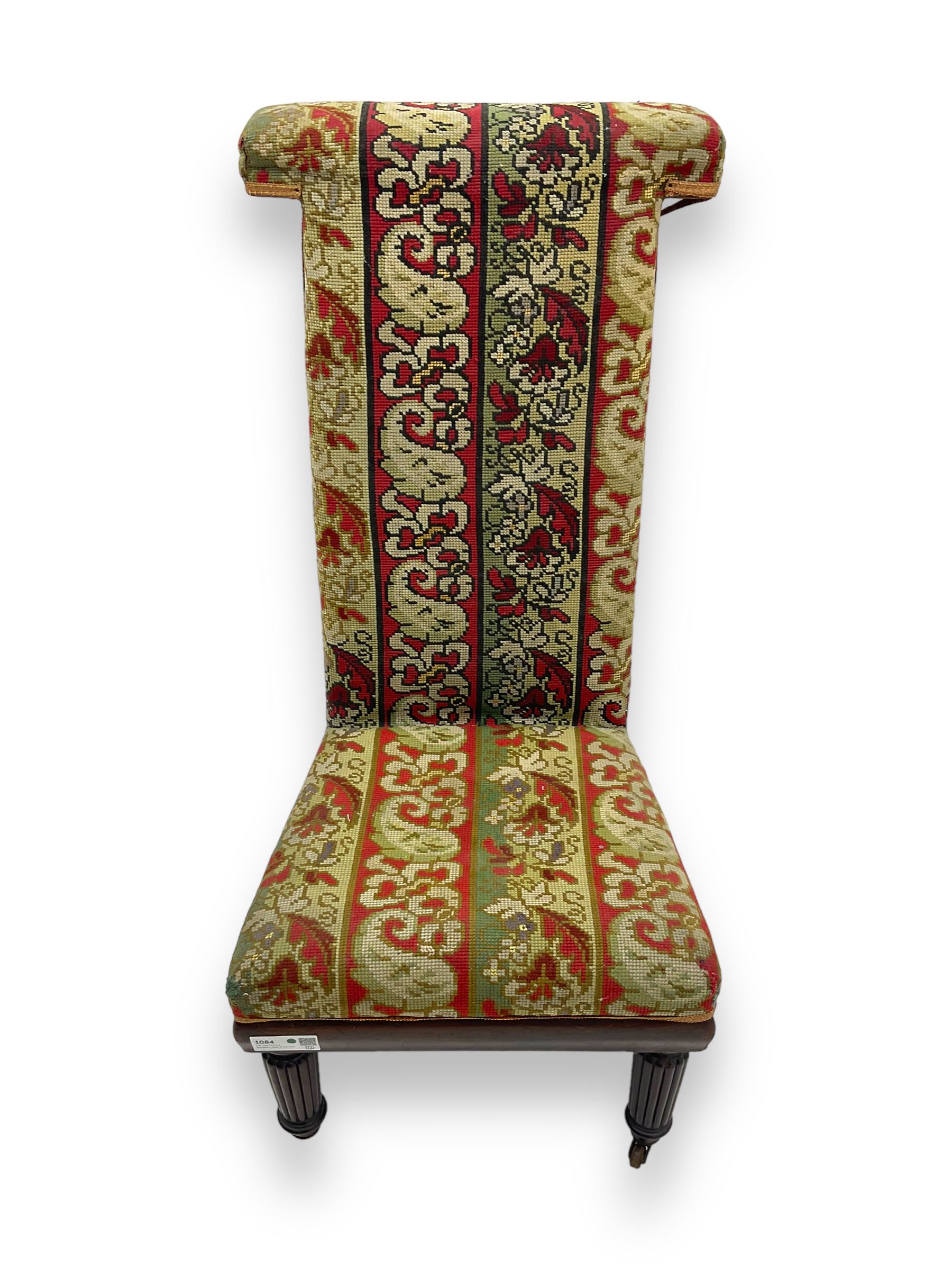 19th century mahogany framed prie-dieu chair, upholstered in red and green patterned fabric, high back with rolled top, standing on turned front supports with castors