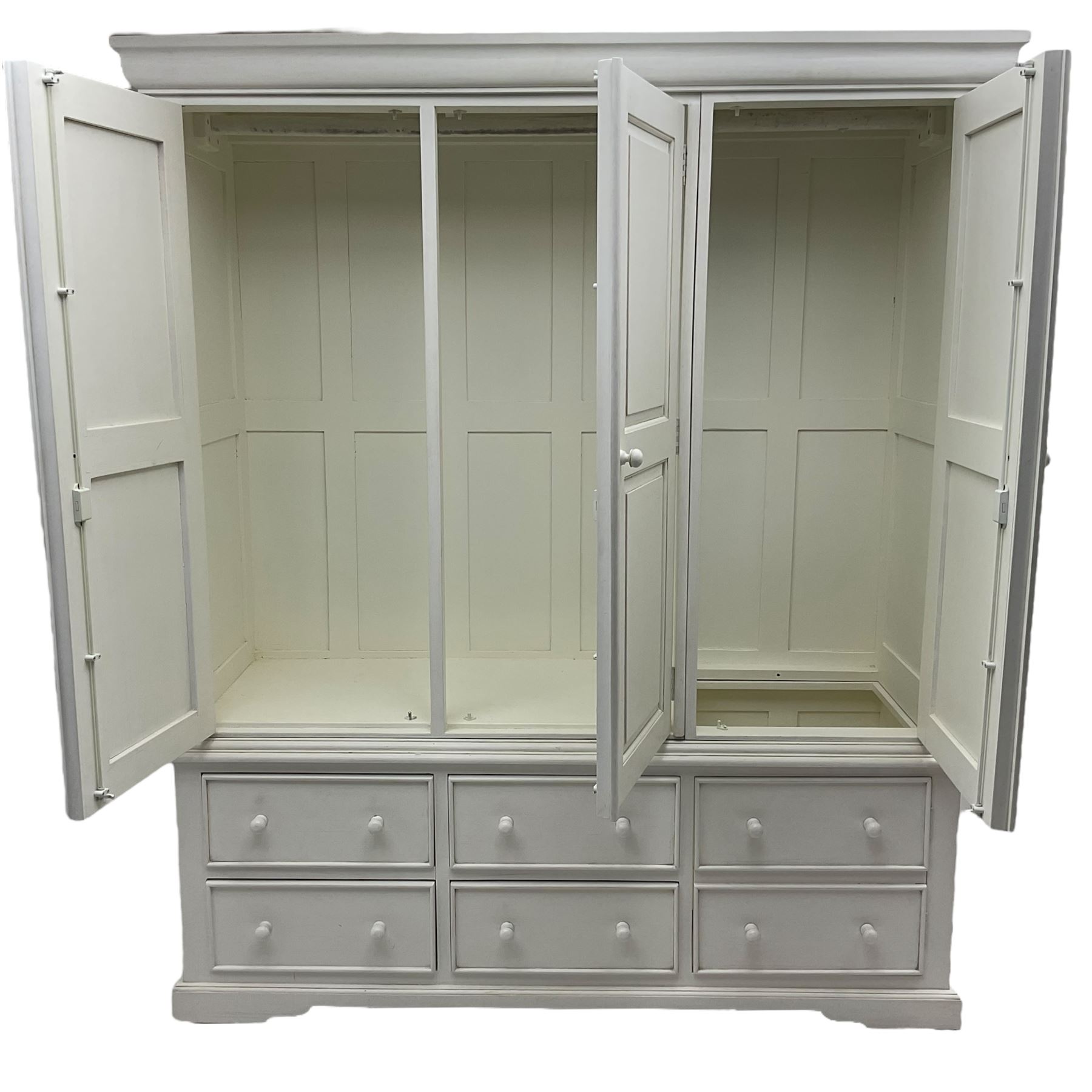 White painted triple wardrobe, projecting moulded cornice over three panelled doors, the interior fitted with hanging rails, four drawers and hinged cupboard to base, on bracket feet