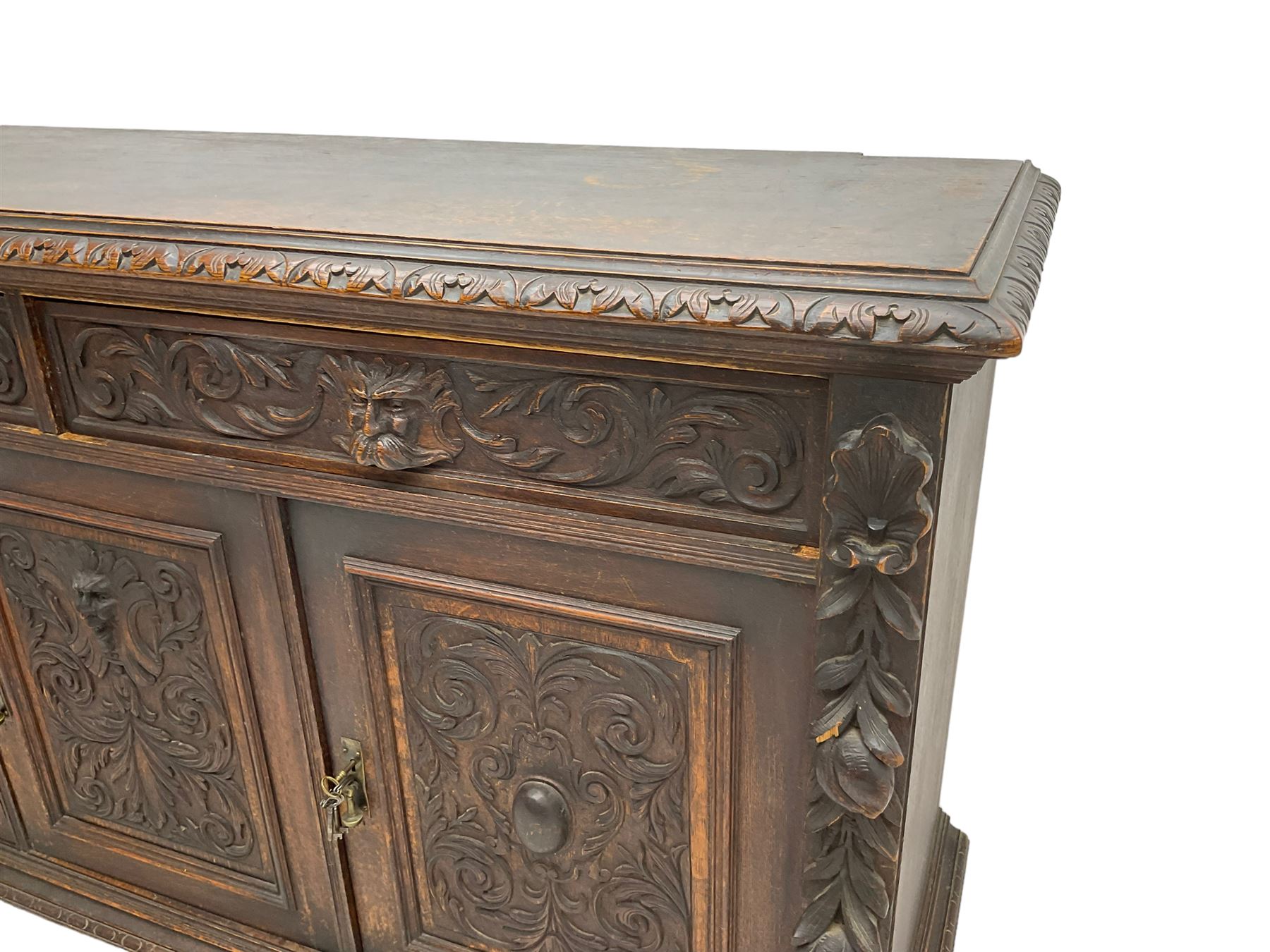 Victorian heavily carved oak sideboard, the moulded top carved with foliate decoration to the edge, fitted with two drawers and three cupboards, the drawer fronts carved with green man mask handles and scrolling foliage, the panelled doors carved with interlacing foliage, on turned compressed bun feet