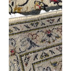 Persian Kashan ivory ground carpet, central medallion decorated with sixteen arranged palmette motifs, within a field decorated with swirling leafy branches and stylised plant motifs, the main border decorated with matching swirling pattern, within floral pattern guard stripes 