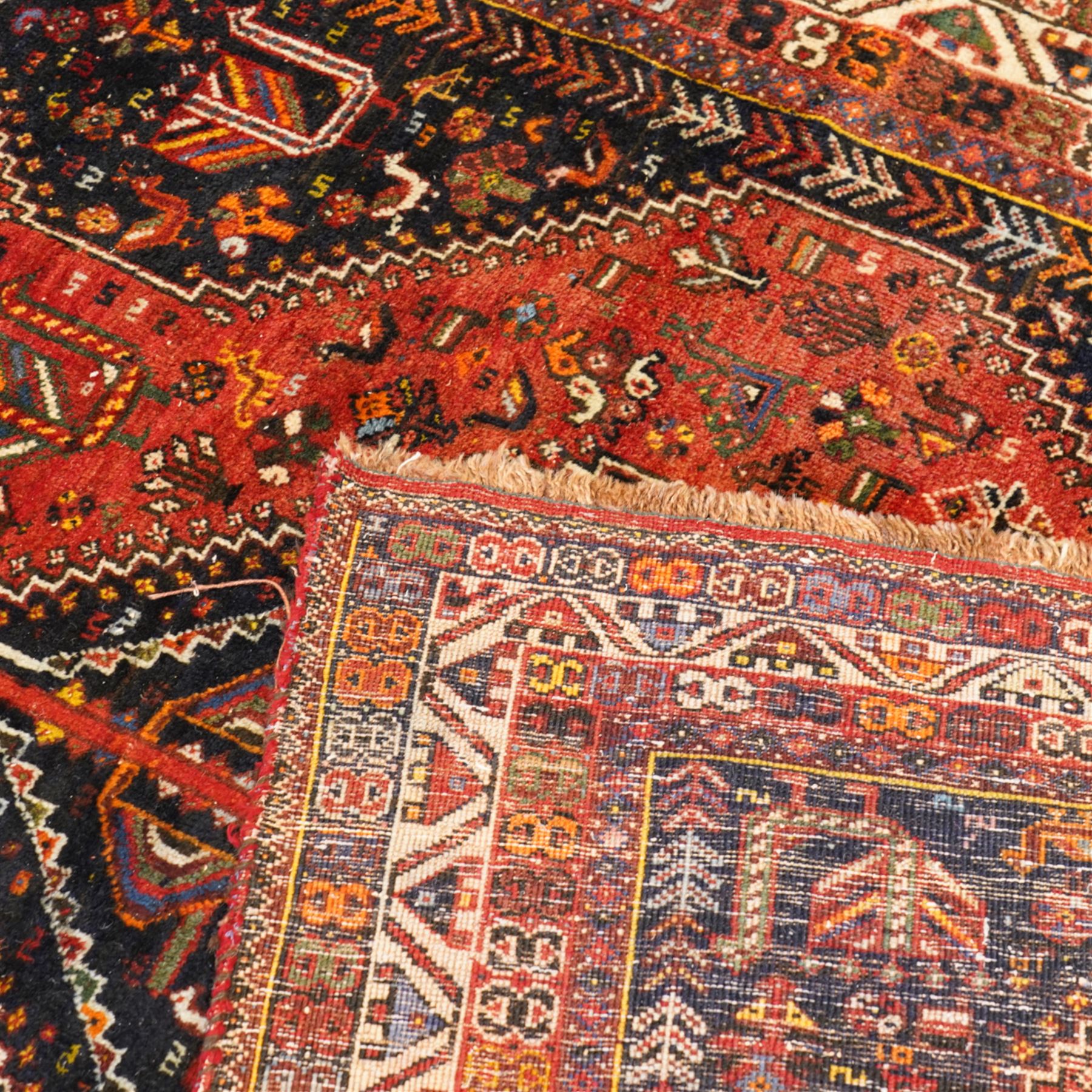 Persian Shiraz crimson ground rug, triple pole medallion surrounded by small stylised motifs depicting birds, animals and plants, within multiple band border each decorated with repeating patterns