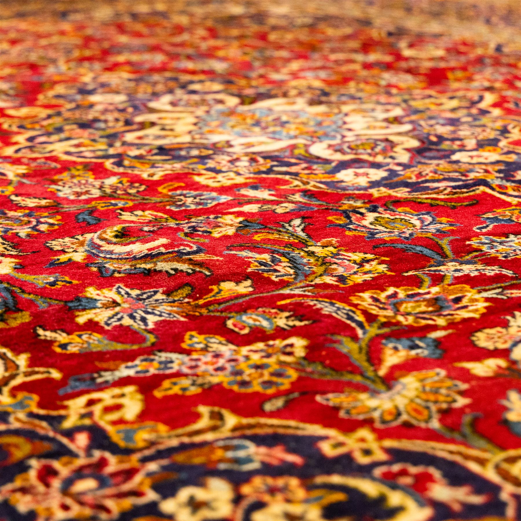 Central Persian Kashan hand-knotted carpet, central field in a ruby red ground with an indigo medallion with pendant motifs, enclosing scrolling arabesques, palmettes, and floral sprays in shades of indigo, turquoise, ivory, and gold, framed by indigo spandrels and a broad floral border between multiple guard stripes 