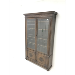 Early 20th century oak bookcase, two lead glazed doors enclosing four shelves above two cupboards, turned supports, W116cm, H184cm, D31cm