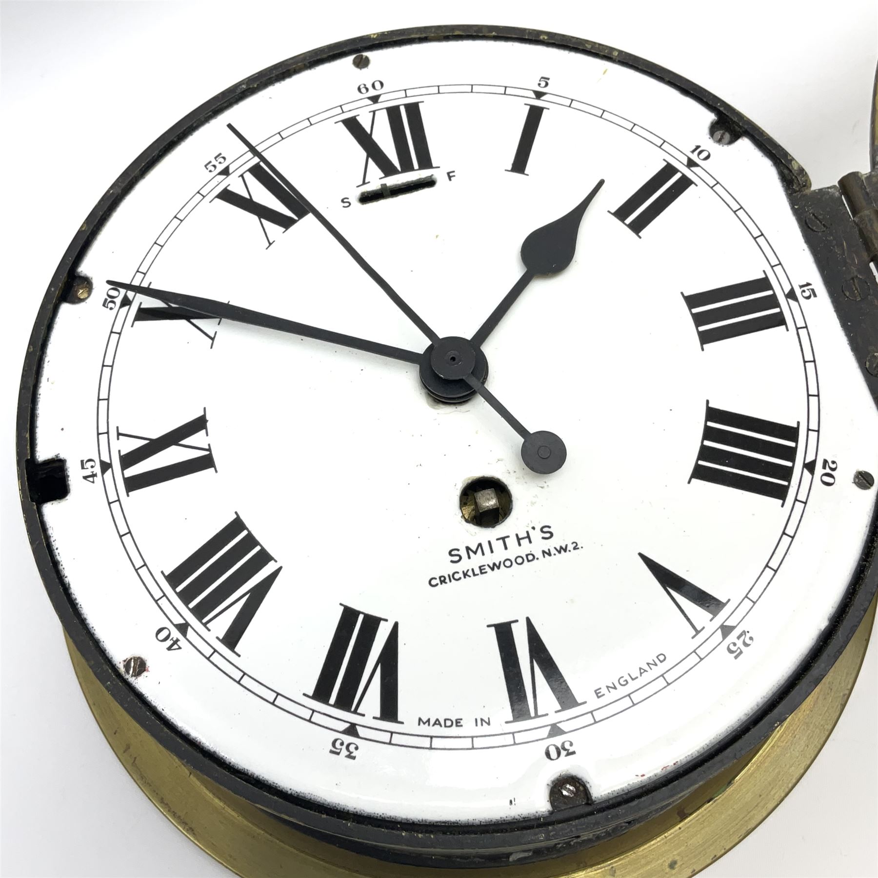 A 20th century Smiths brass cased bulkhead clock with a single train eight-day going barrel movement and balance escapement, white enamel dial with Roman numerals, minute track and five-minute Arabic’s, steel spade hands and centre second hand, dial inscribed “Smiths, Cricklewood N.W, Made in England” brass cast bezel with lock and key, flat glass with silvered sight ring, slow fast balance regulation.
Case diameter 22cm, bezel diameter 19cm.
With key
