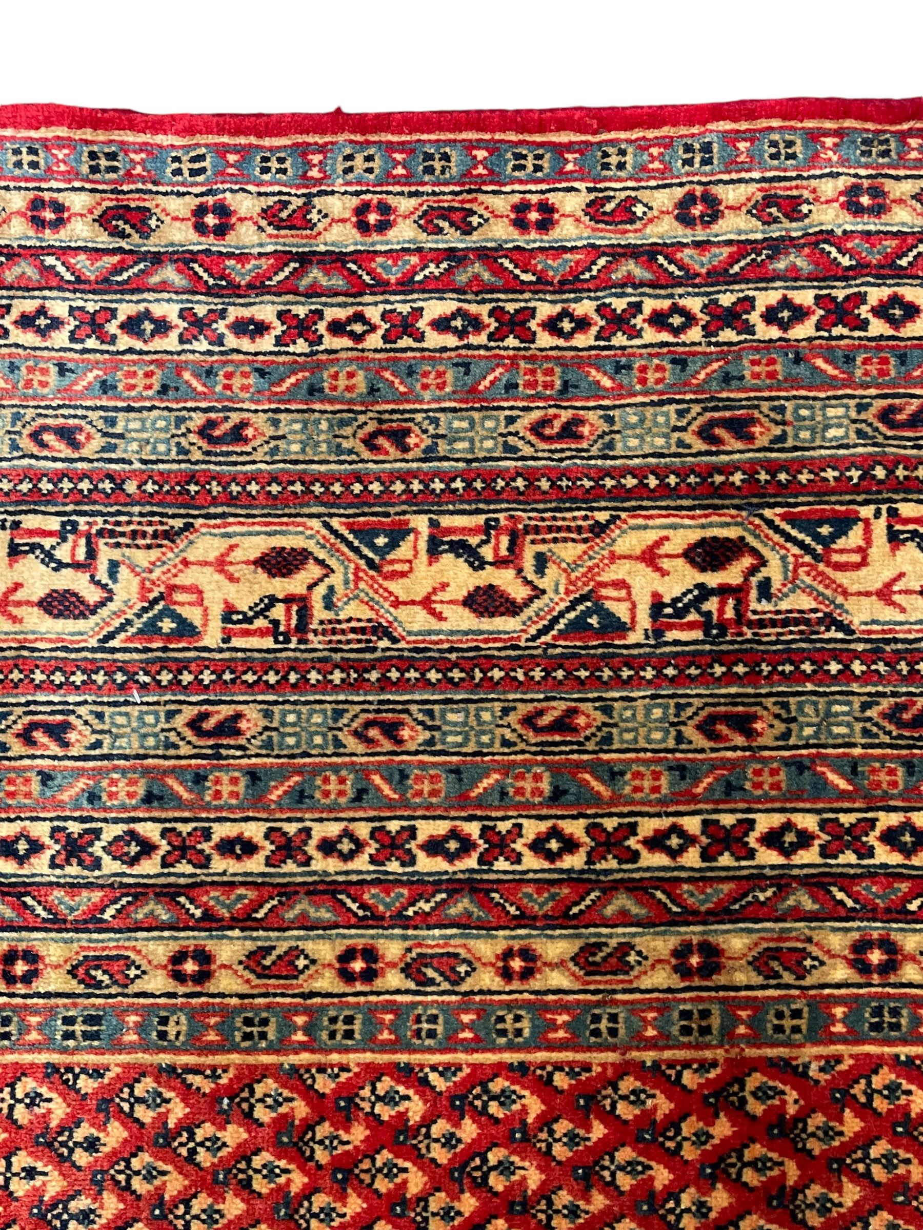 Persian Arak crimson ground carpet, the field decorated profusely with small repeating Boteh motifs, enclosed by multiple border bands decorated with repeating geometric and hook motifs