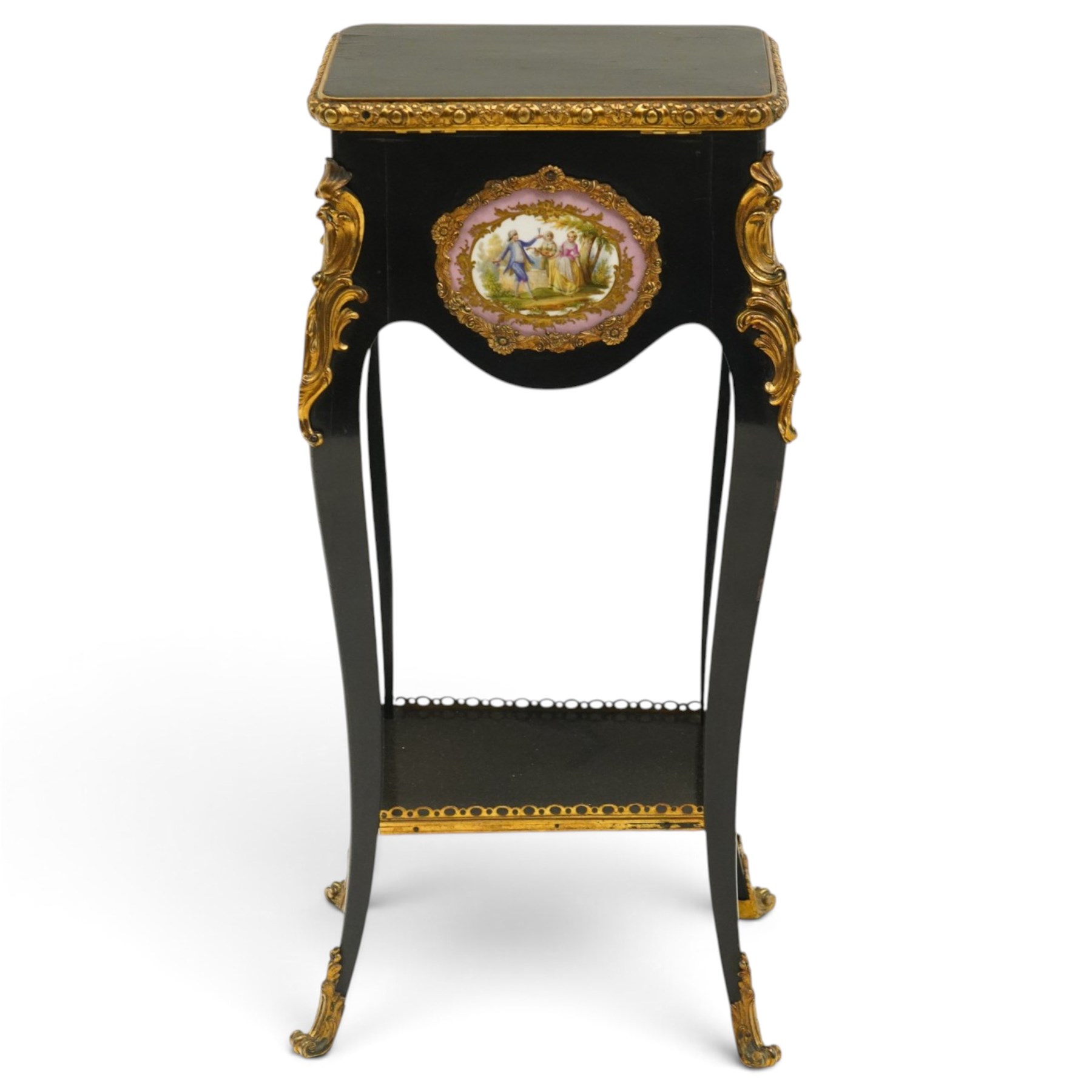 Early 20th century French ebonised sewing or work table, rectangular hinged top with foliate moulded gilt metal edge, enclosing upholstered interior, over a central Sevres style porcelain plaque depicting a courting scene, raised on cabriole supports with gilt metal carotuche and acanthus knee mounts, united by undertier with brass gallery terminating to gilt metal scroll feet