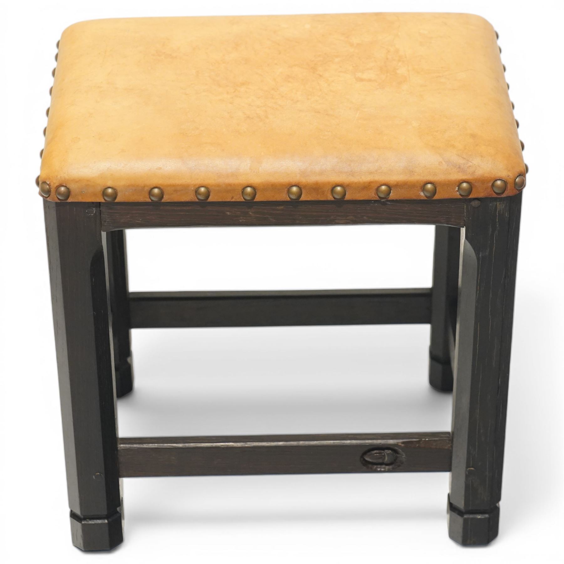 Acornman - dark stained oak stool with upholstered seat, rectangular top with tan leather seat with studded trim, raised on octagonal supports, with carved acorn signature, by the workshop of Alan Grainger of Brandsby