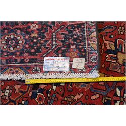 North West Persian Heriz/Ahar hand-knotted carpet, brick red field with a central bold stepped star medallion with pendants, surrounded by angular floral and geometric motifs, ivory spandrels, enclosed by a dark indigo border of stylized rosettes and vine motifs with multiple guard stripes, cotton fringe ends 