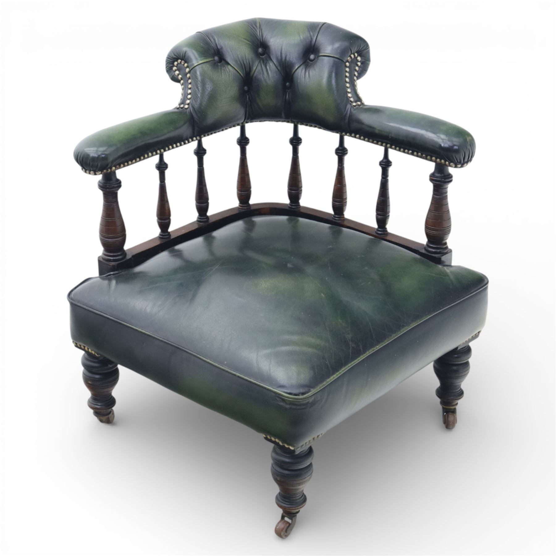 19th century green leather upholstered corner chair, with deep buttoned back and swept padded arms with close studded borders, raised on turned supports united by turned spindles, terminating in brass castors