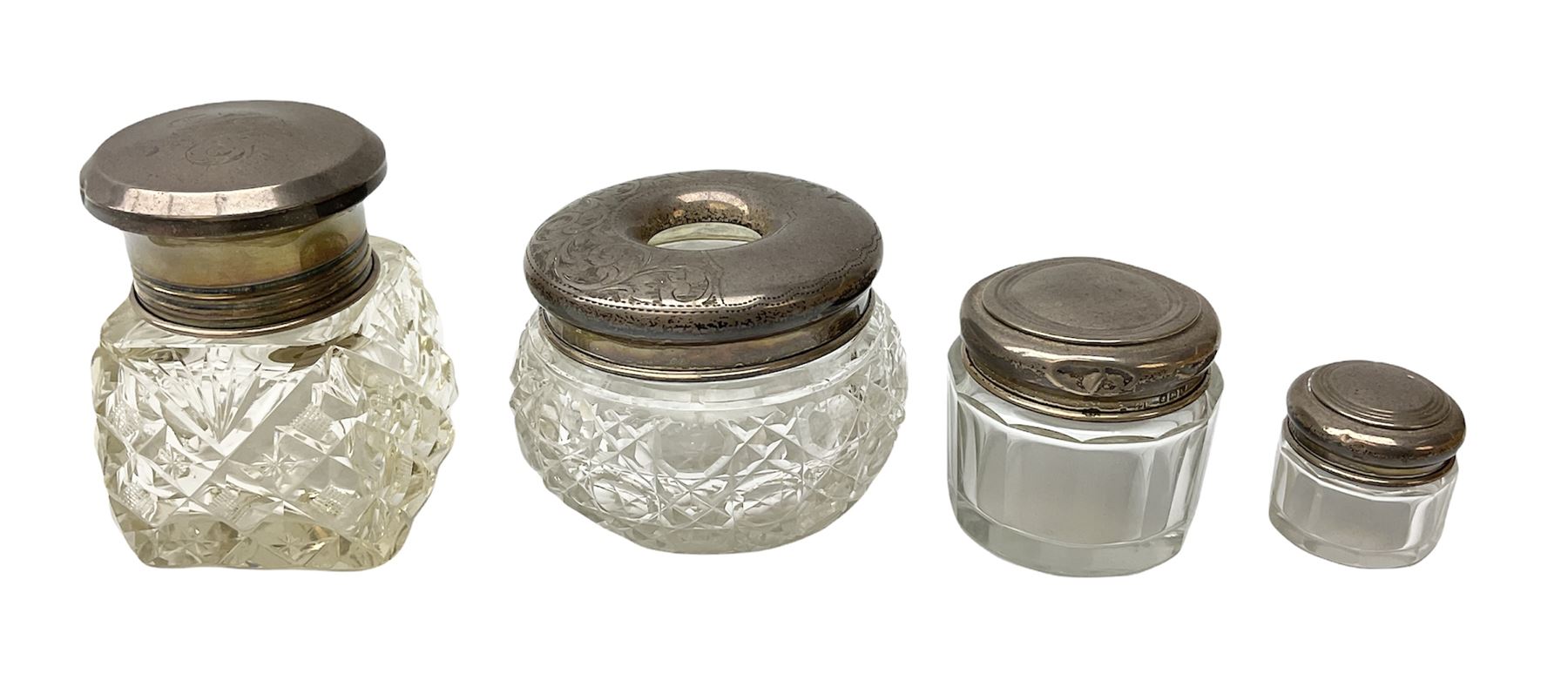 Hallmarked silver top dressing table jars, to include cut glass hobnail example with foliate engraved lid, another 20th century cut glass example with silver engraved screw thread lid, stamped H.S.M Herbert Scott Murdoch, with interior stopper and two smaller glass jars (4)