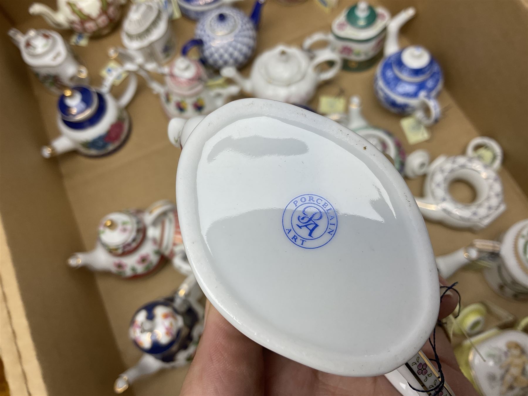 Twenty seven Porcelain Art miniature teapots, with wooden display together with a collection of other ceramics and glassware etc, including Goebel Hummel collectors plates, in three boxes,
