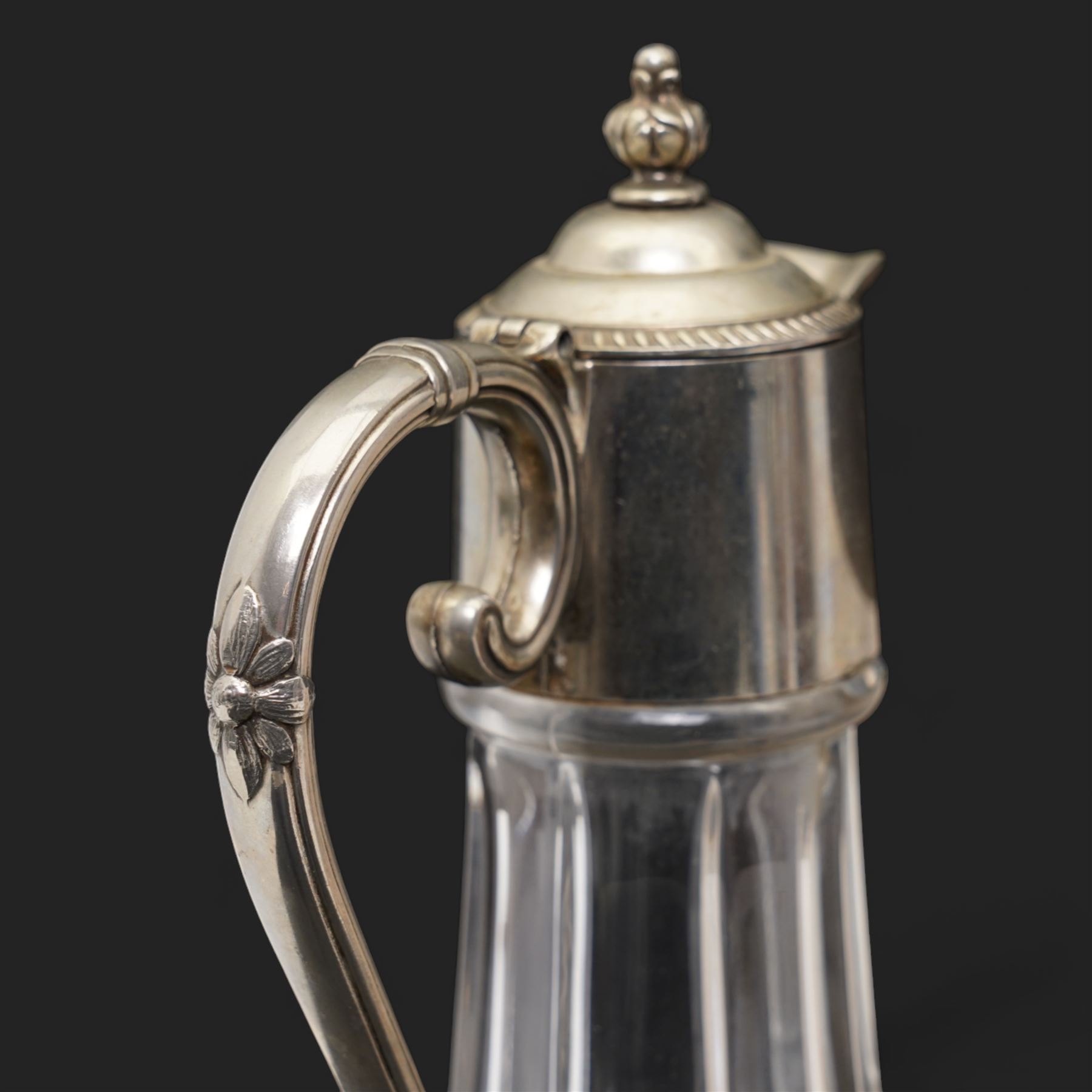 Composite plaque, depicting Sprites in a garden, with inset 'Arts and Commerce Promoted' medallion to reverse, 20cm x 33cm; together with a moulded glass Claret jug with silver plated mount H30cm 