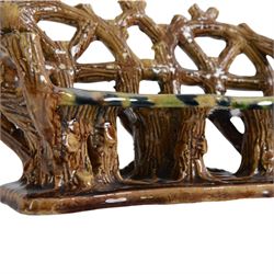 19th century pottery model of a bench, possibly Skey Pottery Tamworth, Staffordshire, the shaped seat mottled in shades of green, dark blue, yellow and brown, supported upon naturalistically modelled tree stumps, the arms and back modelled as intertwined branches, H14cm W21cm D10cm