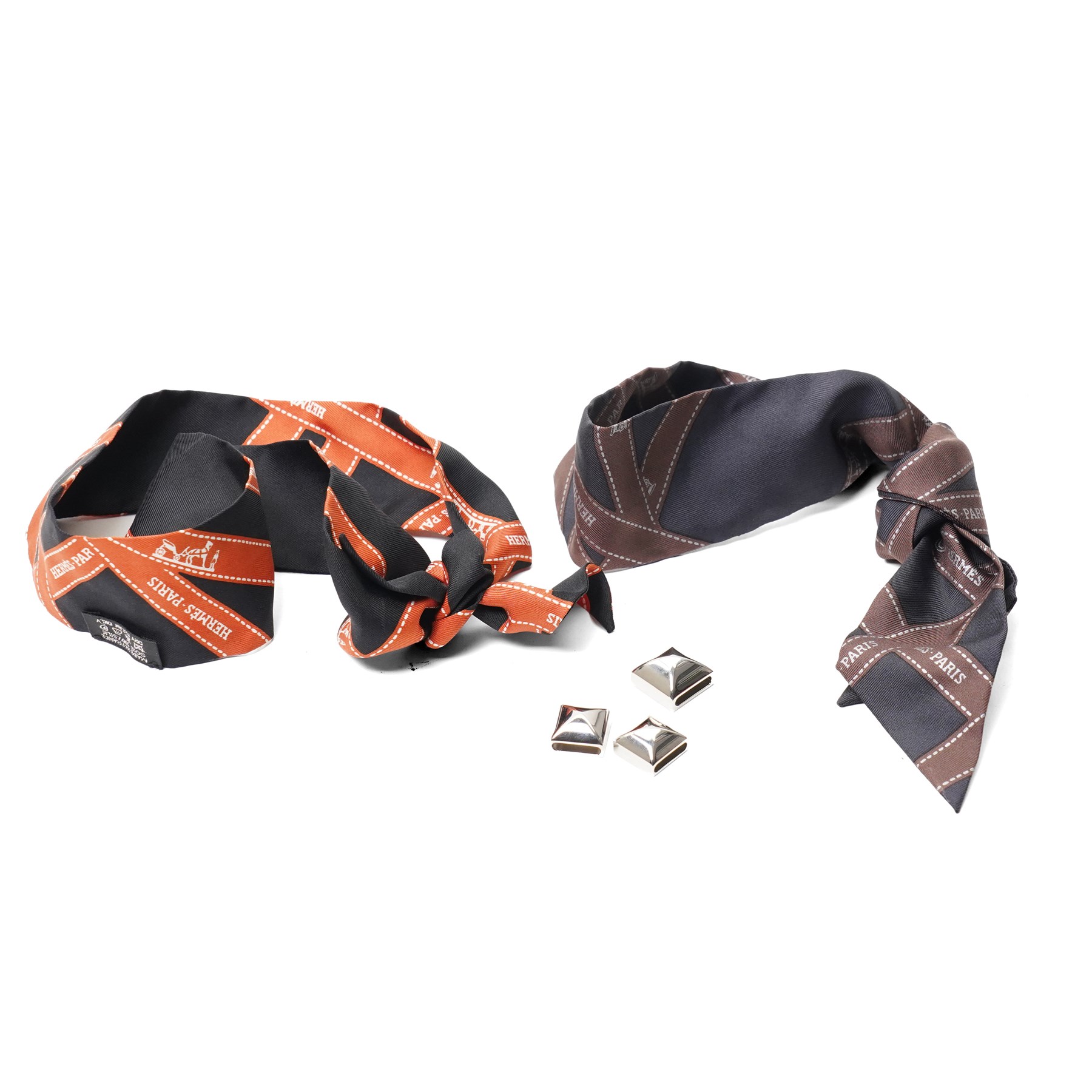 Hermès - two ‘Bolduc’ silk Twilly scarves, in orange/black and navy/brown colourways, together with three palladium-tone Médor pyramid Twilly scarf rings, with original dust bag and cylindrical box