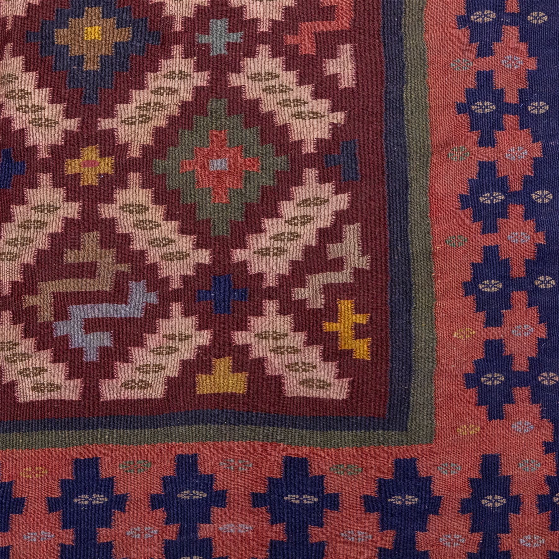 South West Persian Qashgai flatweave kilim, field decorated with a repeating diagonal lattice of stepped lozenges and angular hooked motifs, interspersed with small tribal devices, woven is shade of madder red, soft pink, indigo blue, ochre, and olive green, framed by a narrow geometric border and contrasting guard stripes 