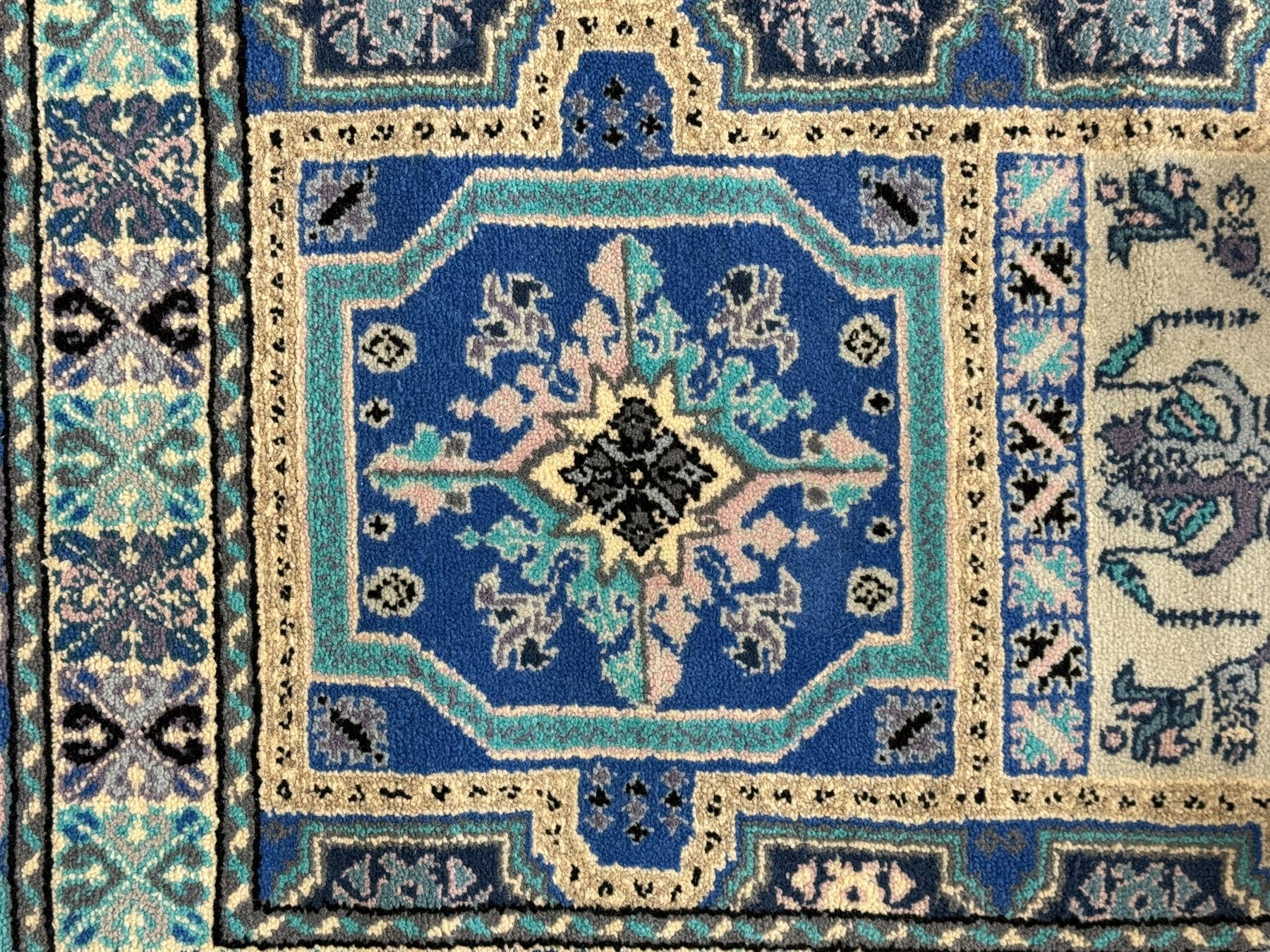 Morrocan single weft blue ground rug, the field segmented into a grid of ten rectangular panels, bordered by a series of guard bands with repeating floral and geometric patterns with interlocking vines and rosettes, the edges finished with a fringe of twisted tassles