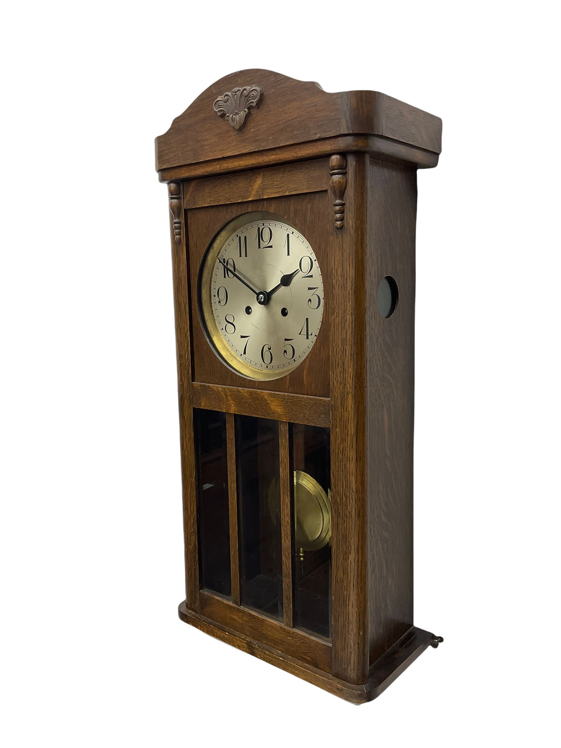 A 1930's wall clock in an oak case with a full-length door, three glazed panels and visible pendulum, case with a shaped pediment and applied carving, 6'' silvered dial with Arabic numerals, minute track and steel baton hands, eight day going barrel movement striking the hours on a gong.

	



