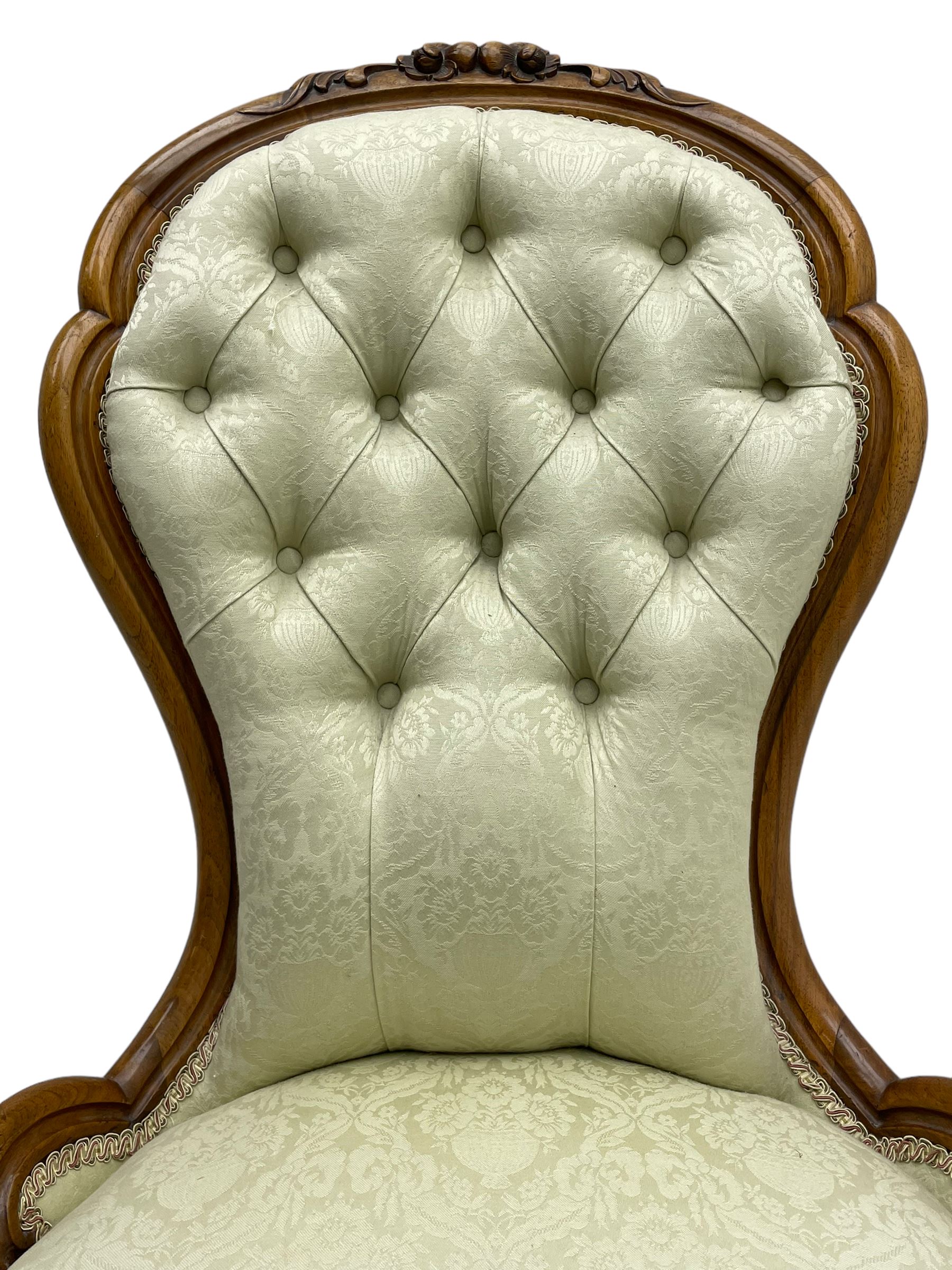 Victorian walnut framed nursing chair, the cresting rail decorated with carved applied flower heads and acanthus leaves, shaped back and sprung seat upholstered in buttoned ivory damask fabric, serpentine front over cartouche carved cabriole supports with ceramic castors (W57cm H92cm); with matched footstool, circular top over shaped moulded apron, on floral carved cabriole feet (W34cm) 