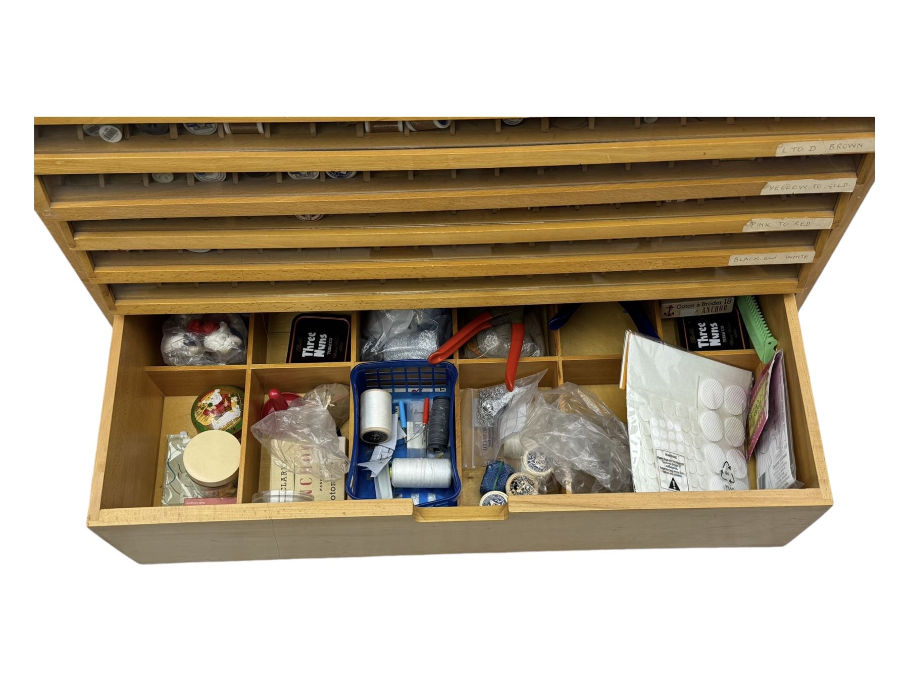 Large beech haberdashery thread storage cabinet, rectangular form with fourteen glass-fronted sloping drawers housing an extensive array of thread spools in assorted colours, over two larger drawers, raised on plinth base