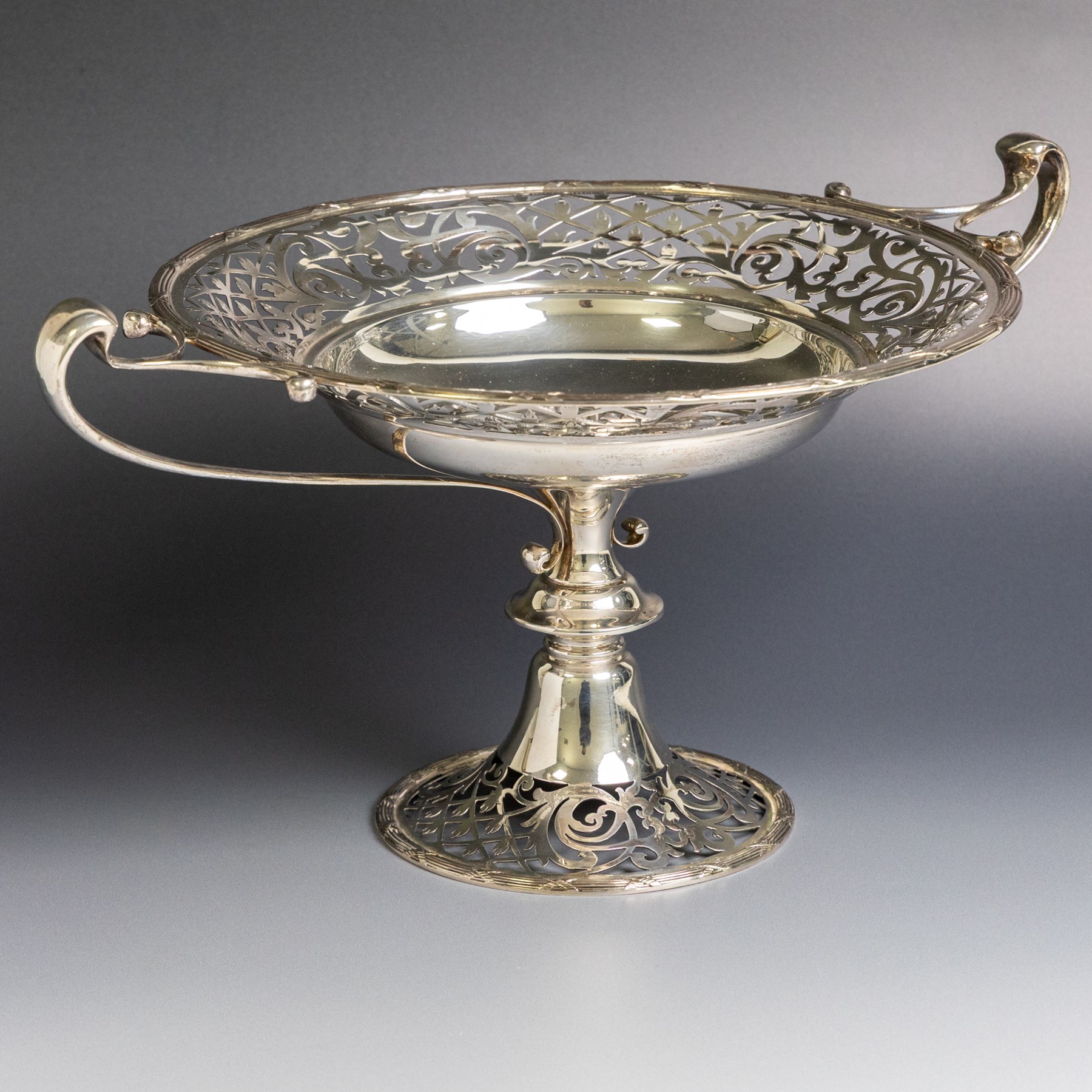 Early 20th century silver twin handled tazza, the bowl of circular form with pierced foliate decoration and ribbon and reed border, with two whiplash curved handles, upon a knopped stem and pieced foliate foot, hallmarked Walker & Hall, Sheffield 1911, H20cm