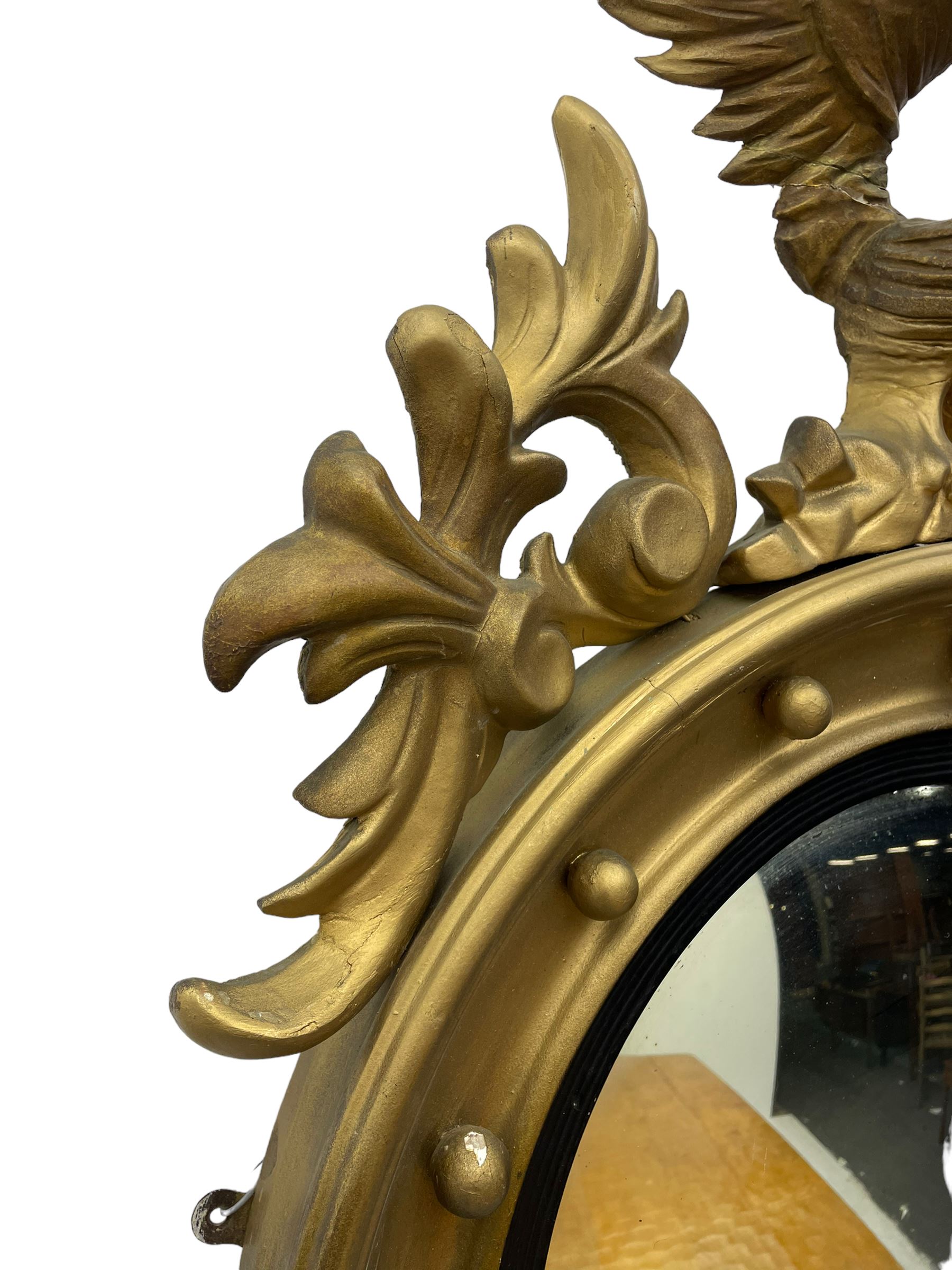 Pair of Regency period giltwood convex wall mirrors, moulded circular frame decorated with spherical mounts surmounted by a carved eagle with spread wings, foliage scroll carved upper and lower brackets, reed moulded and ebonised slip enclosed convex mirror plate 