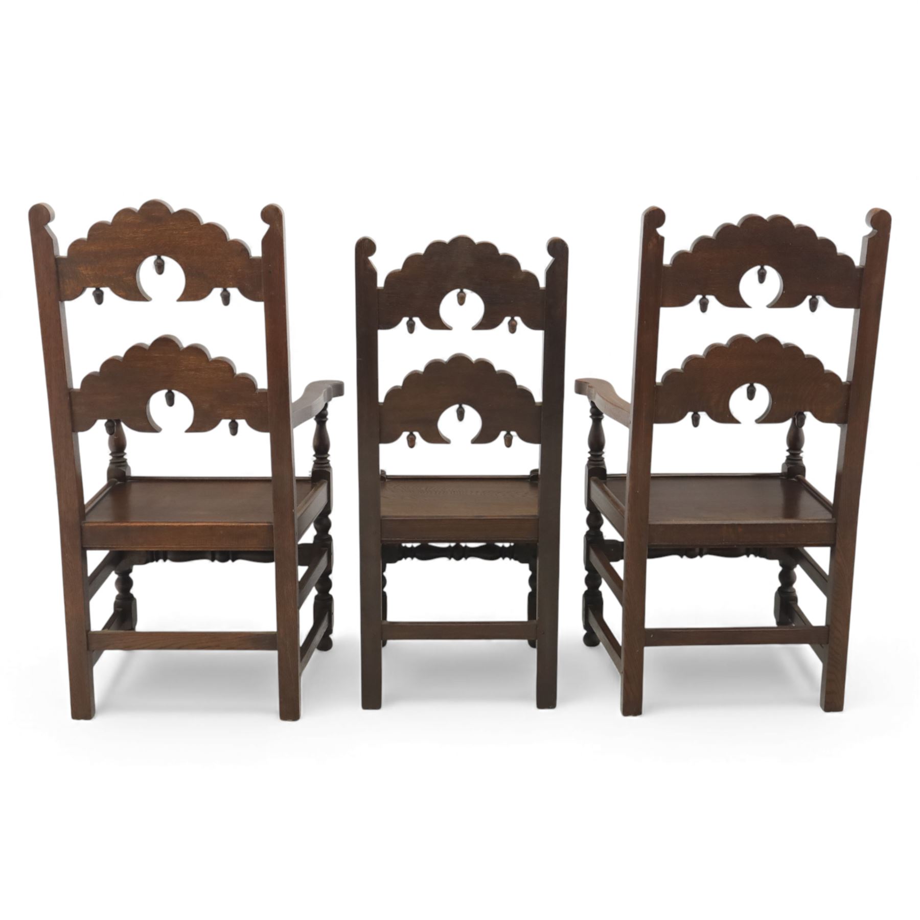 Early 20th century set of seven Jacobean Revival oak chairs, comprising pair of cavers and five chairs, each with carved mask and scroll decoration to the crest and and back rail, plain oak seat, upon turned front legs and block rear legs with conforming stretchers