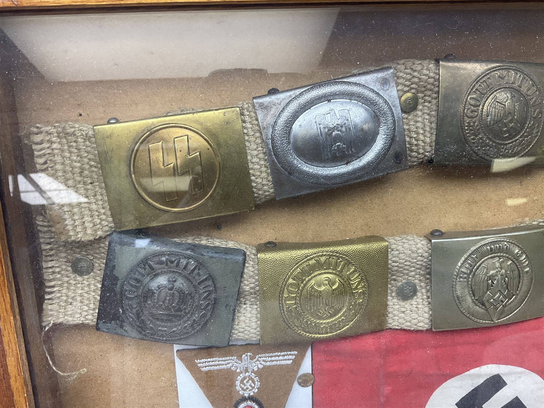 Display of eleven German belt buckles including 'SS', Party Buckle, two Army, Fire Service, two Luftwaffe, NSKK, Hitler Youth and WW1 Army; framed with three cloth badges and an armband