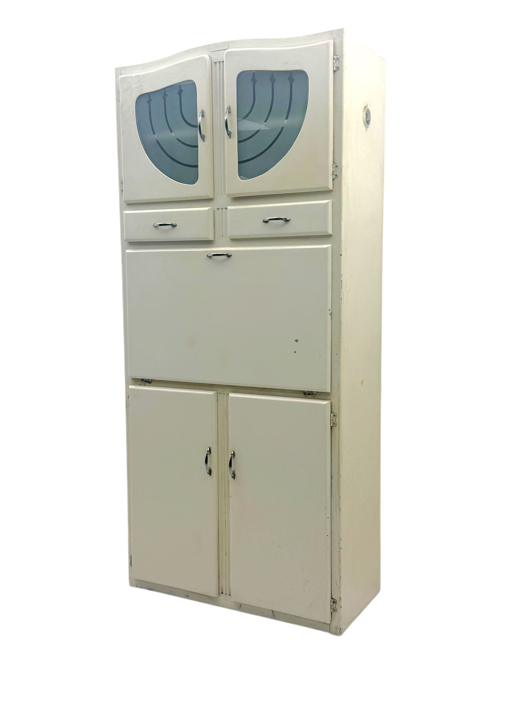 Mid-20th century painted kitchen cabinet, moulded top above a pair of glazed cupboard doors with stylised arrow motif panels, over two drawers and a fall-front cupboard, the lower section with twin cupboard doors