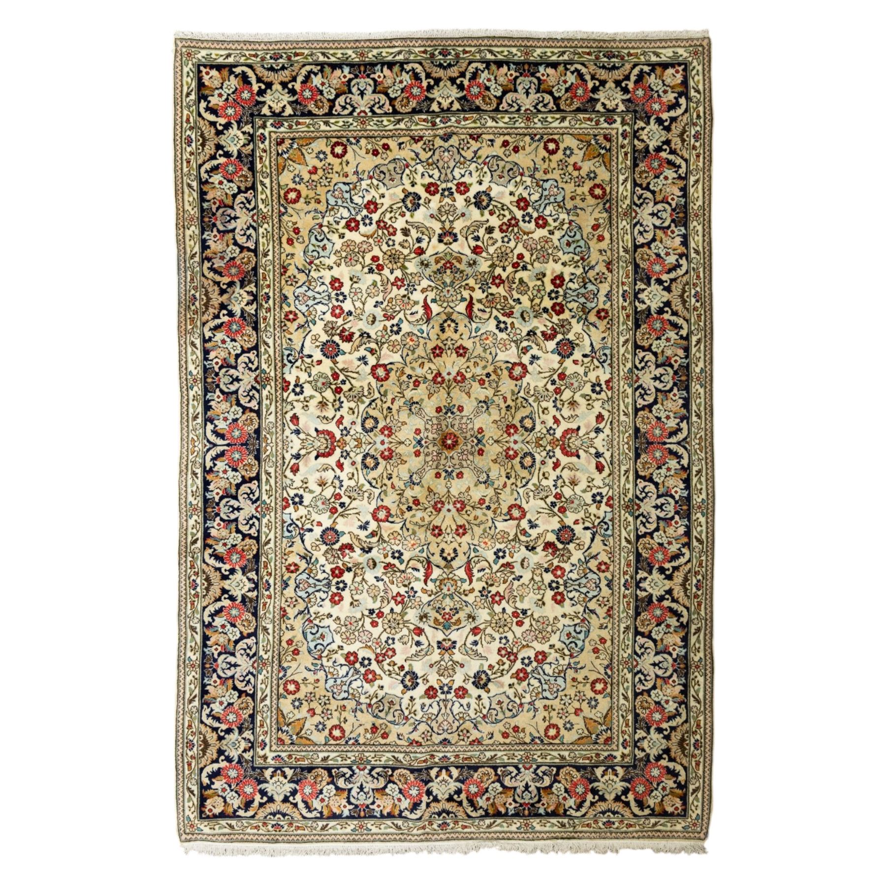 Central Persian Kashan hand-knotted carpet, ivory ground, with an all-over floral field centred by a subtle shaped medallion, surrounded by scrolling foliate and floral motifs incorporating rosettes, palmettes and delicate vine work, enclosed by a dark navy border with repeating palmettes and meandering vines, flanked by floral guard stripes, with cotton fringes