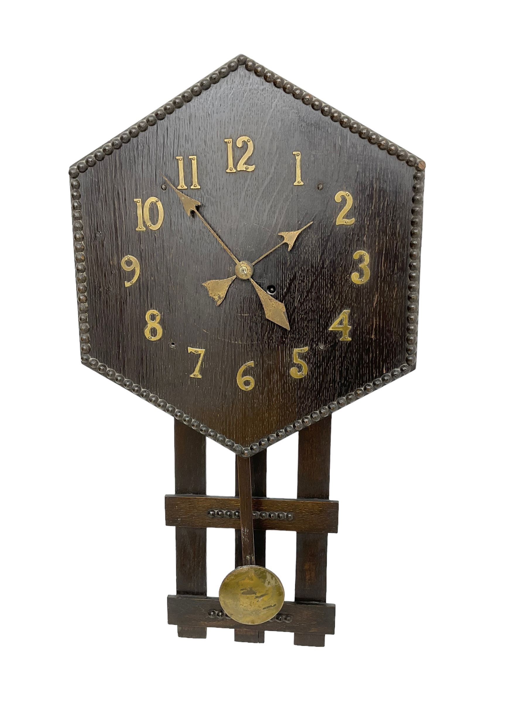 1920’s Art deco drop dial wall clock - with an eight day spring driven timepiece movement, hexagon dial in dark oak with applied brass Arabic numerals and arrow shaped hands, open framework backboard, visible wooden pendulum with a brass faced bob.