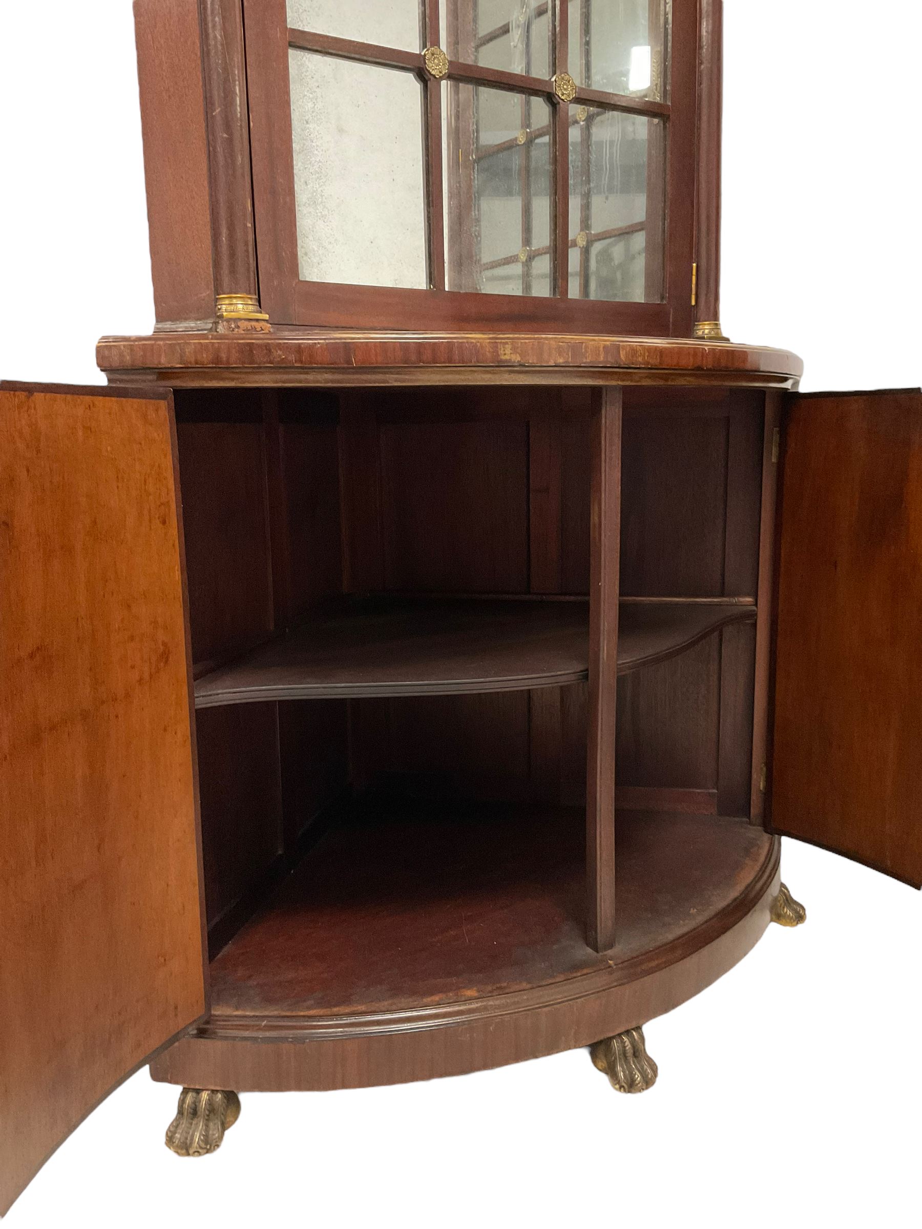 Pair of French Empire design corner cabinets, the straight-front upper section with canted corners and applied half-column pilasters, enclosed by mirror glazed door, the bow-front lower section enclosed by two doors with applied mouldings, mounted by cast metal floral rosettes, skirted base with cast gilt metal hairy paw brass feet