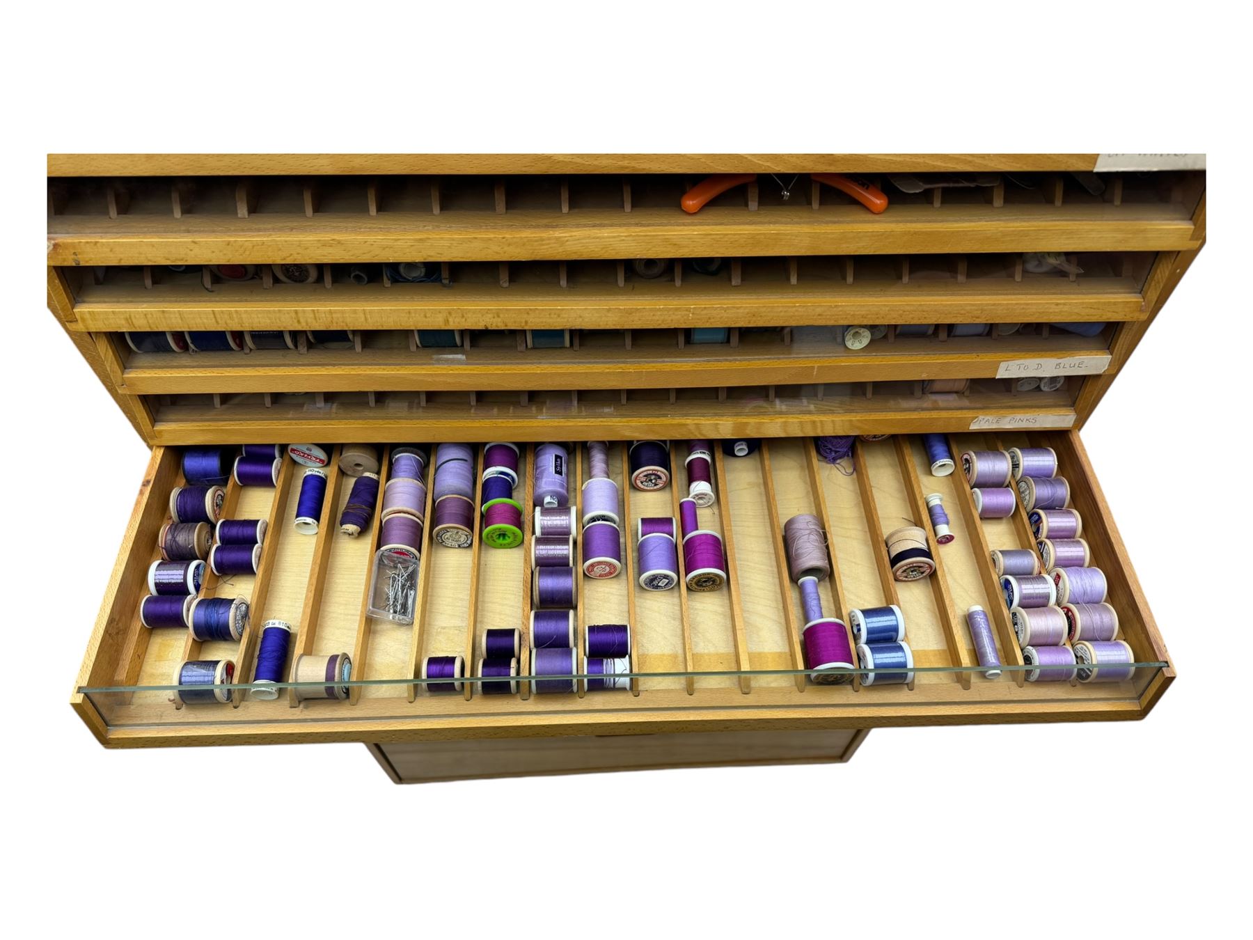 Large beech haberdashery thread storage cabinet, rectangular form with fourteen glass-fronted sloping drawers housing an extensive array of thread spools in assorted colours, over two larger drawers, raised on plinth base