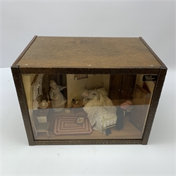A 1/12th scale diorama of a cottage bedroom, depicting an elderly couple, he in bed, her by the door with cup in hand, the interior furnished with wash stand, wash jug and bowl, needle work, brass bed, and mouse trap under chair, plus light up candle and ceiling pendants, etc., H29cm L40cm D26cm.

