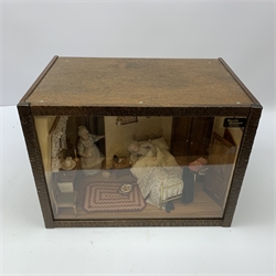 A 1/12th scale diorama of a cottage bedroom, depicting an elderly couple, he in bed, her by the door with cup in hand, the interior furnished with wash stand, wash jug and bowl, needle work, brass bed, and mouse trap under chair, plus light up candle and ceiling pendants, etc., H29cm L40cm D26cm.

