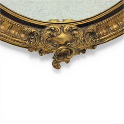 Rococo Revival style gilt composition oval wall mirror, moulded oval frame with fluted and beaded bands enclosing a bevelled mirror plate, the outer frame with acanthus leaf and scroll carved cresting to each side