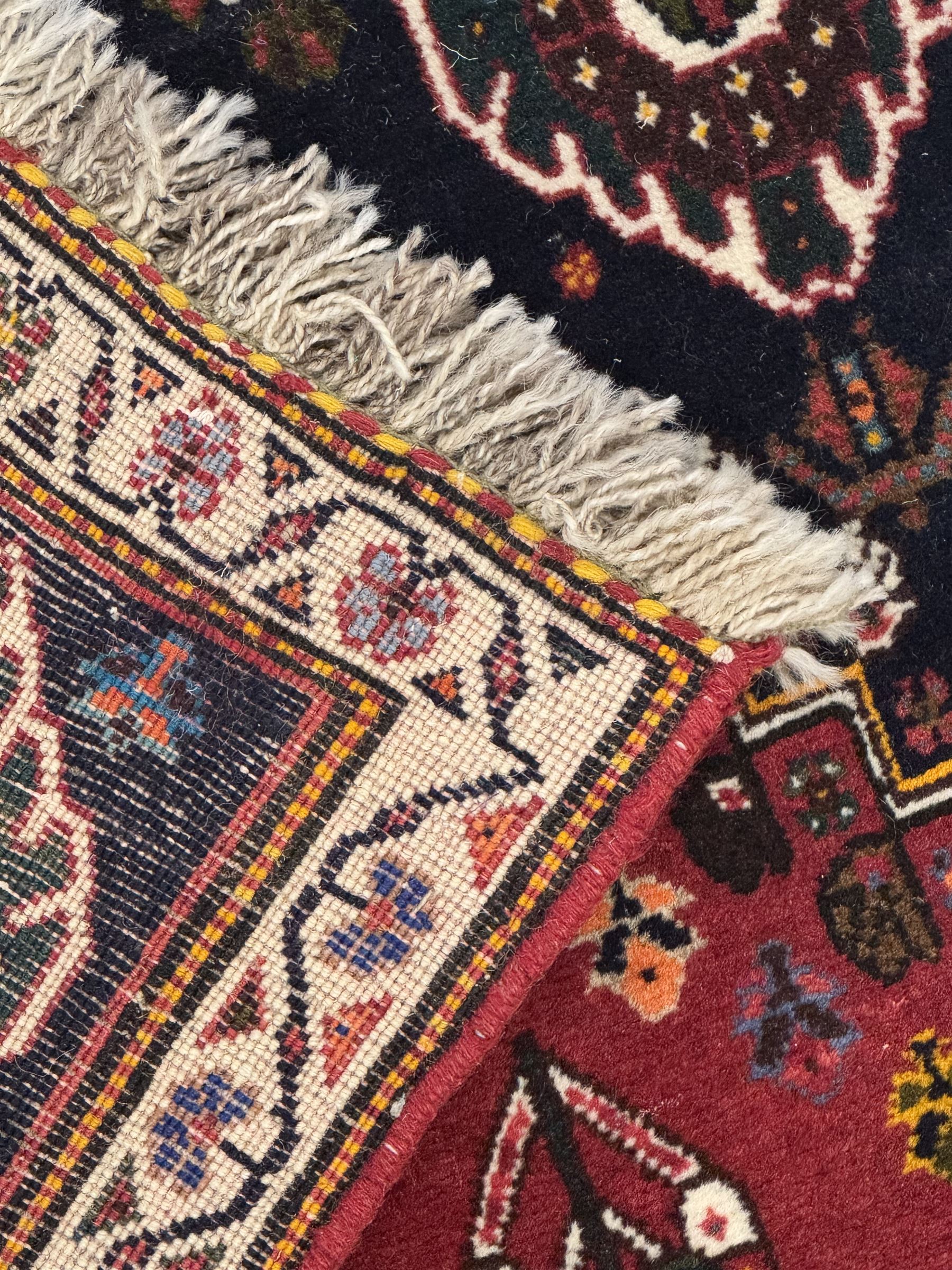 Persian Qashqai crimson ground runner, the field decorated with repeating diamond-shaped medallions flanked by angular floral motifs, the spandrels with intricate boteh designs, framed by an ivory border with stylised floral patterns and scrolling vines