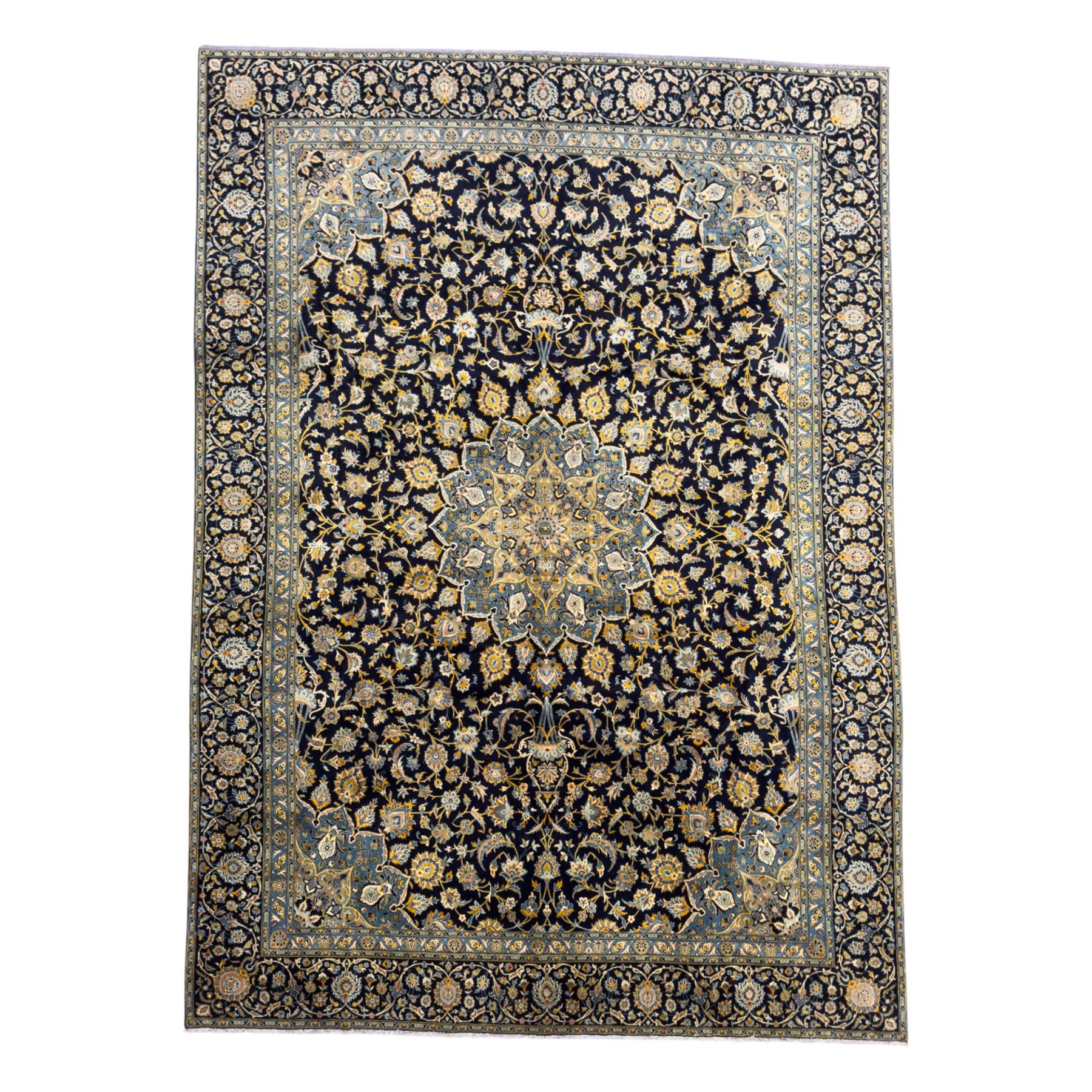 Central Persian Kashan hand-knotted carpet, the navy field with central medallion in pale blue and gold tones, surrounded by spiralling arabesques and palmettes, framed by quarter spandrels and a wide border of stylised lotus and rosette motifs between floral guard stripes, from the region of Kashan