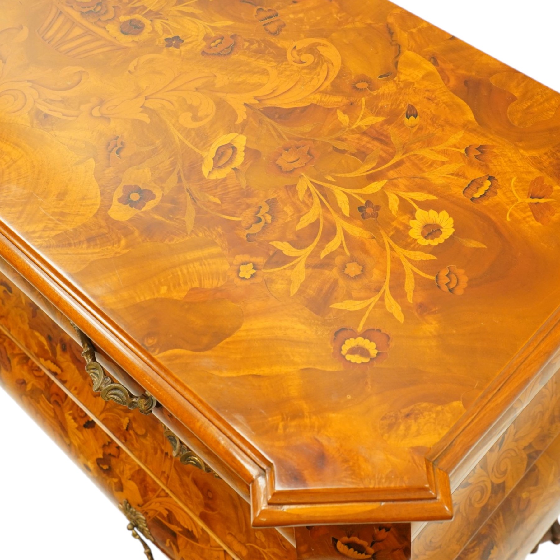 Colombo Mobili - Italian walnut and floral marquetry bombé commode chest, rectangular top with canted eared corners inlaid with urn motif and trailing scrolling foliage, fitted with three long graduating drawers with gilt metal handles, profusely inlaid with scrolling acanthus leaves interspersed with urns and cartouches, on large carved ball-and-claw feet