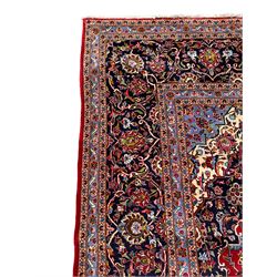 Persian Kashan crimson ground carpet, floral pattern indigo ground central medallion and matching spandrels, the field decorated densely with scrolling foliate patterns and floral motifs, the main border decorated with scrolling branches and palmettes, within floral pattern guard stripes
