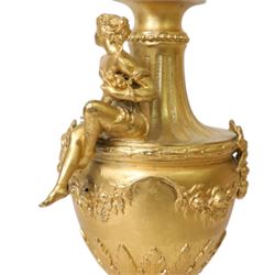 Pair of Rococo style gilt metal table lamps, the urn shaped bodies each with applied figure seated upon shoulder, and female mask to opposite side issuing scroll leading to top of neck, the body cast and applied with stiff leaf detail, and foliate swags and wreaths, upon square pink marble plinths with applied gilt metal mask mounts, and four gilt metal bracket feet, each supported a pleated cream silk closed top lampshade, H63cm
