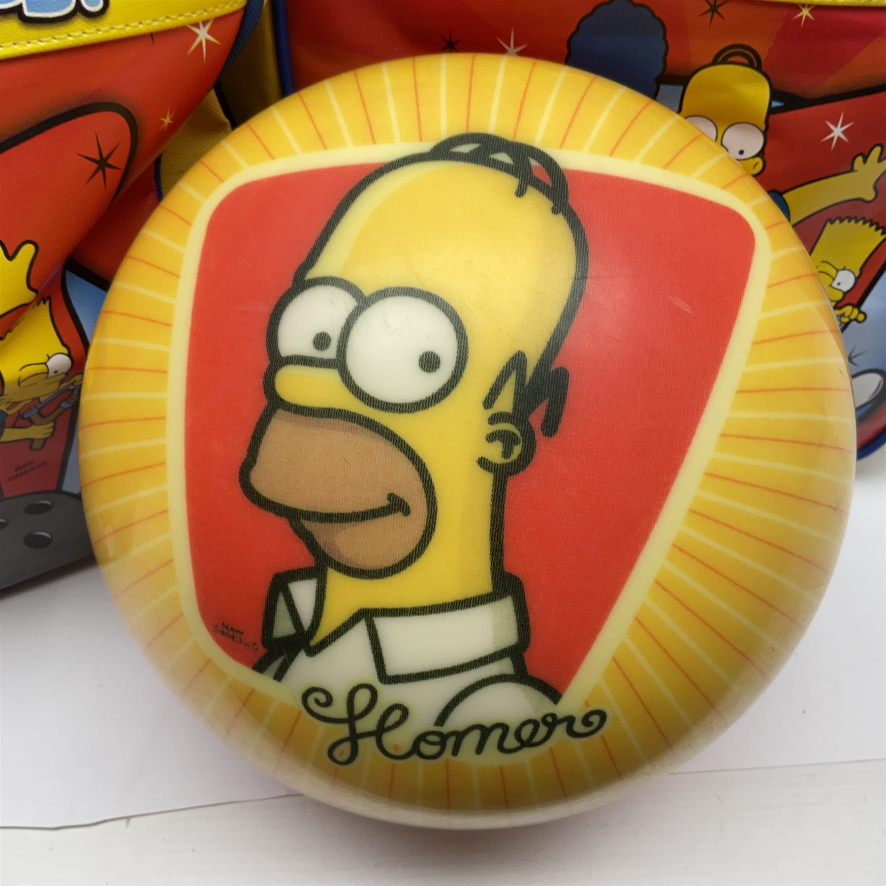 Two The Simpsons 'The Bowling Club' tenpin bowling balls, the first an undrilled example depicting Bart Simpson on a green ground, the second a drilled example depicting the Simpsons family on an orange ground, both in Simpsons The Bowling Club bags, together with a Disney Monsters, Inc. tenpin bowling ball, in matching bag and a Maxim tenpin bowling ball
