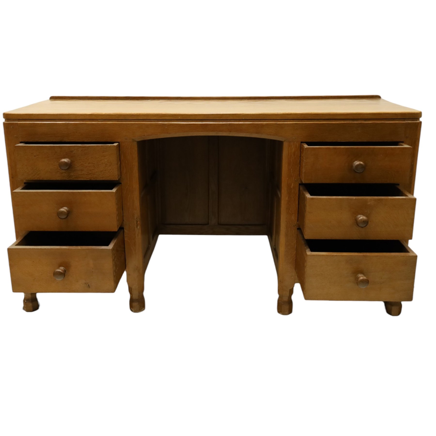 Mouseman - adzed oak kneehole dressing table or desk, the rectangular adzed top with raised back and canted corners, over an arched recessed kneehole flanked by three graduating drawers to each side with turned knob handles, raised on octagonal feet, with carved mouse signature, by the workshop of Robert Thompson of Kilburn