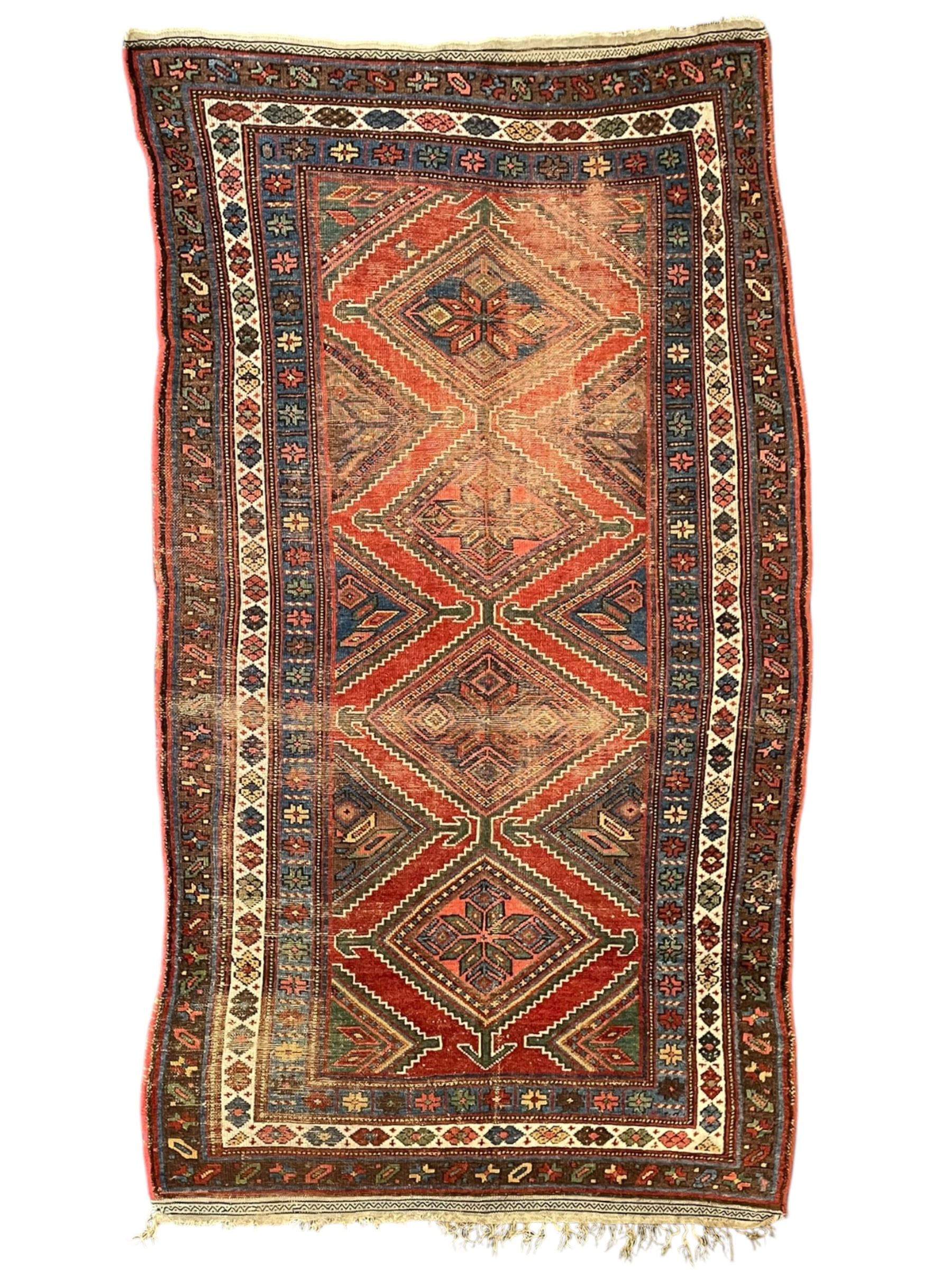 Kurdish crimson ground rug, the field decorated with four lozenge medallions, triple band border decorated with stylised flower heads