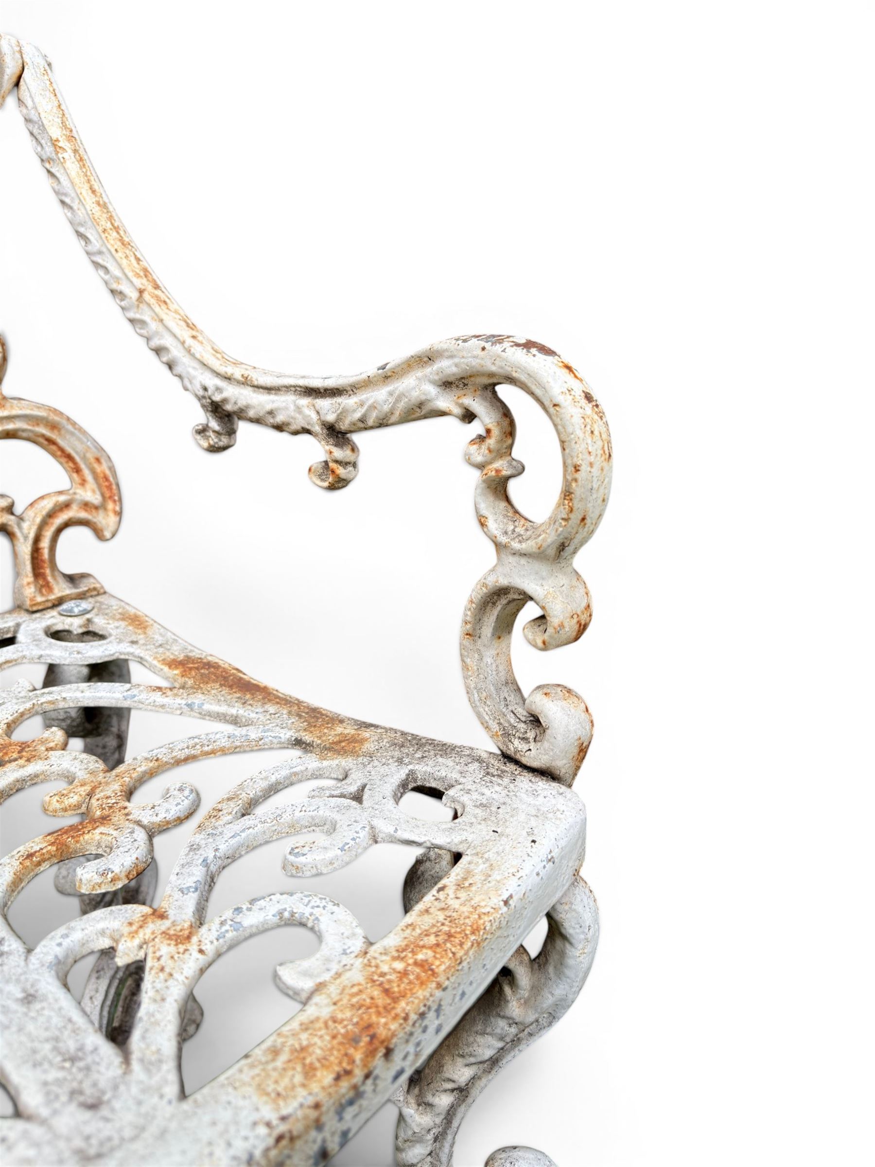 Pair of Victorian cast iron garden chairs, the ornate pierced back of scrolling foliate design, scrolling arm terminals over splayed supports formed of C and S-scrolls, in distressed white painted finish
